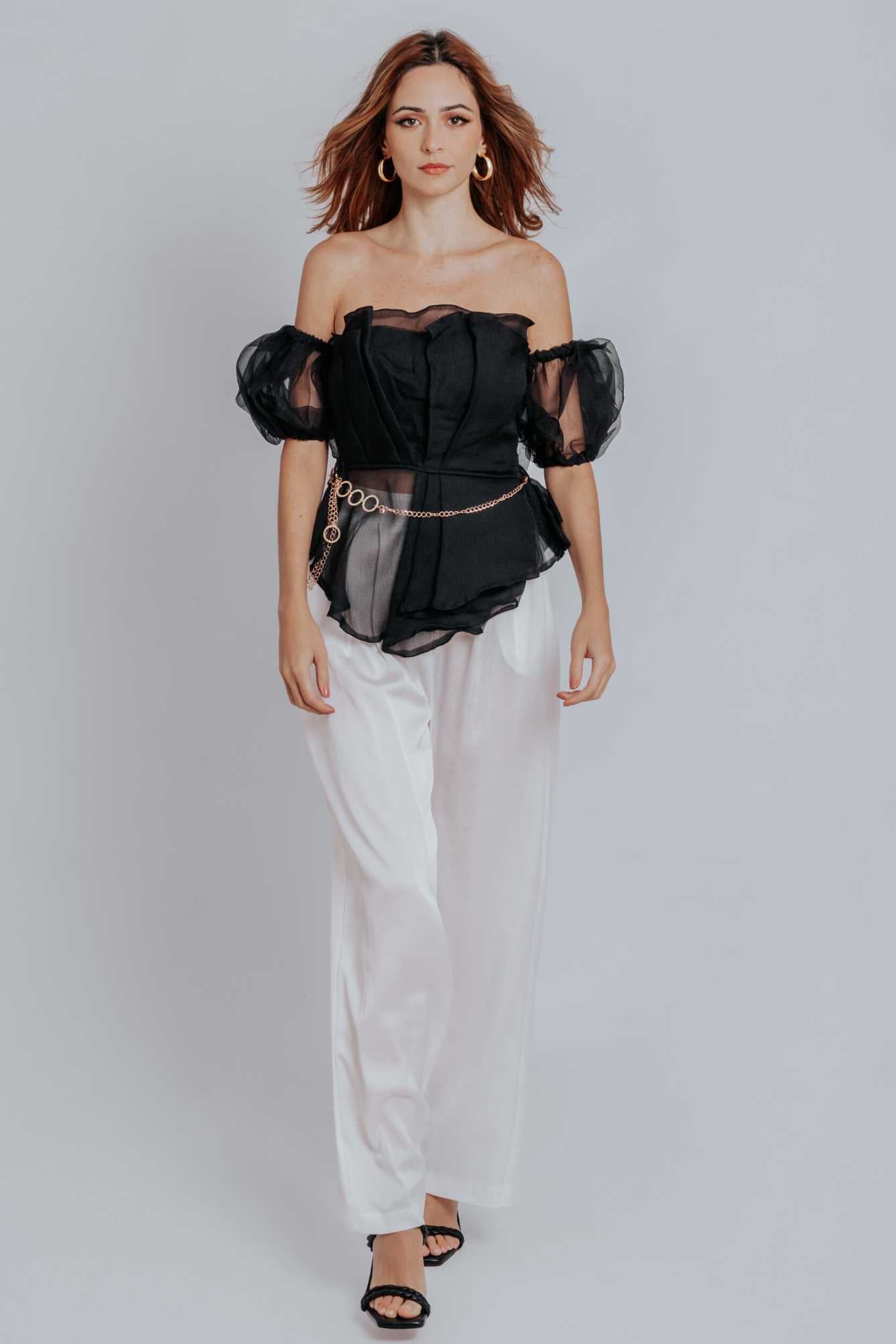 Raven Peplum Top featuring off-the-shoulder neckline and pleated bodice, styled with trousers and heels.