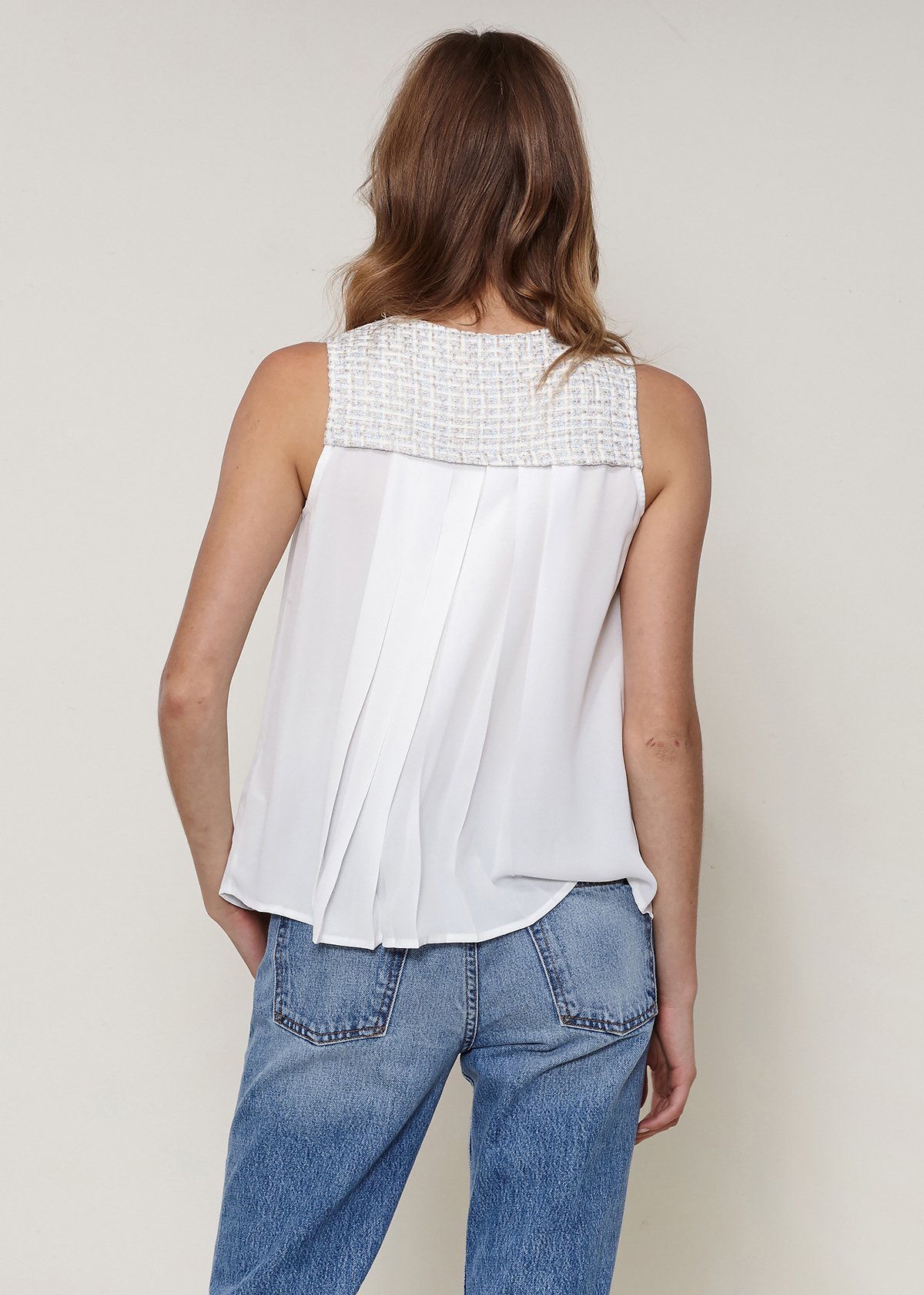 Women's sleeveless ivory tweed blouse with pleated front and button fly closure, showcasing elegant design and texture.