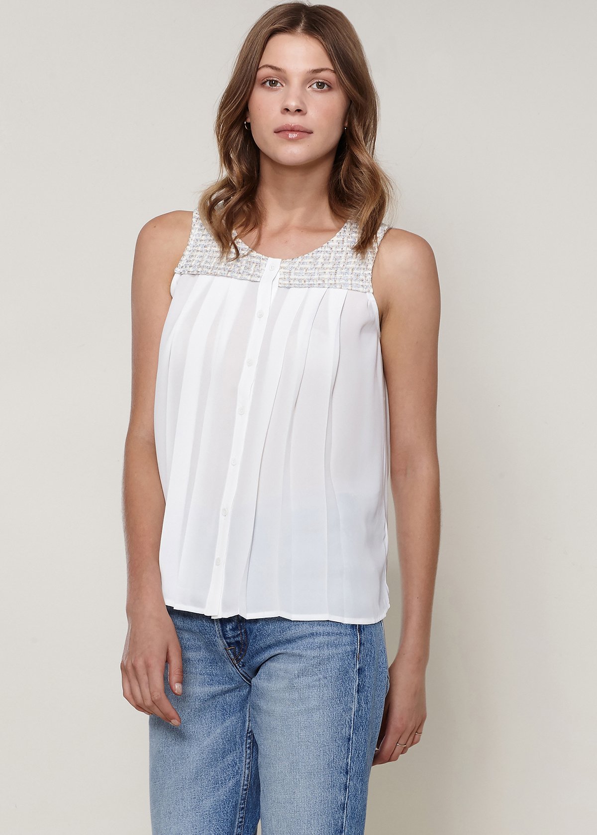 Women's sleeveless ivory tweed blouse with pleated front and button fly closure, showcasing elegant design and texture.