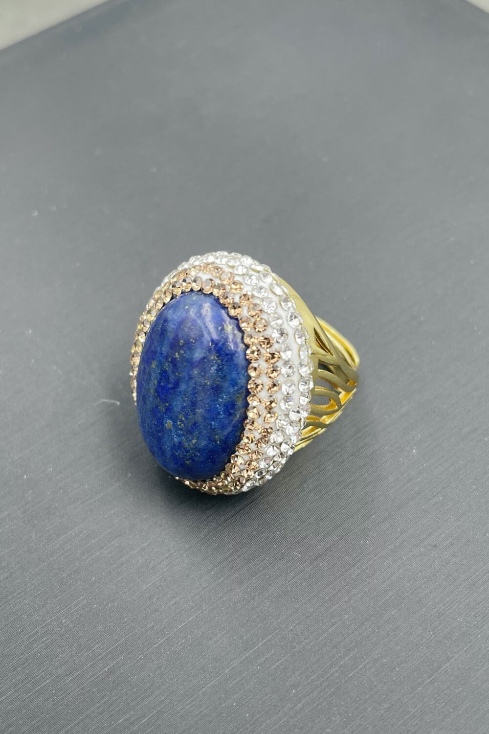 A flat lay image of a 24K gold-plated rhinestone ring featuring a minimalist design with lapis lazuli stone.