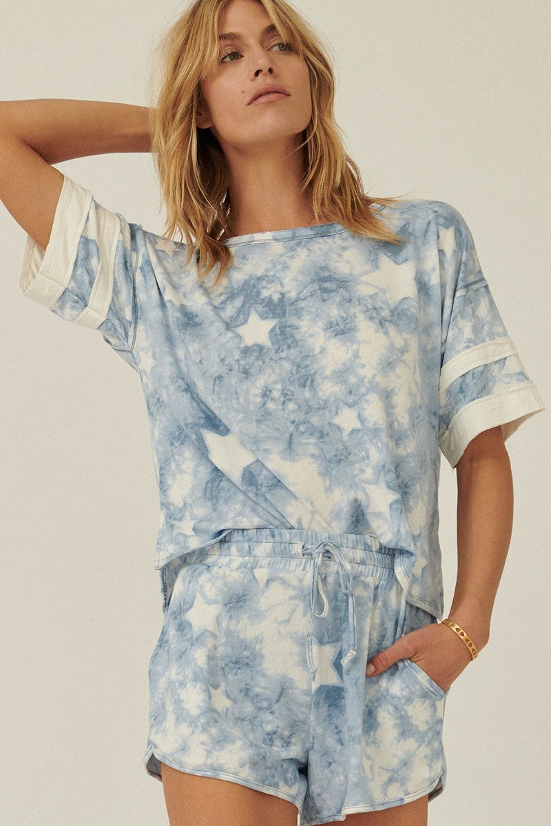 A blue star-pattern tie-dye knit top with short sleeves and varsity stripe trim, showcasing a relaxed oversized fit.