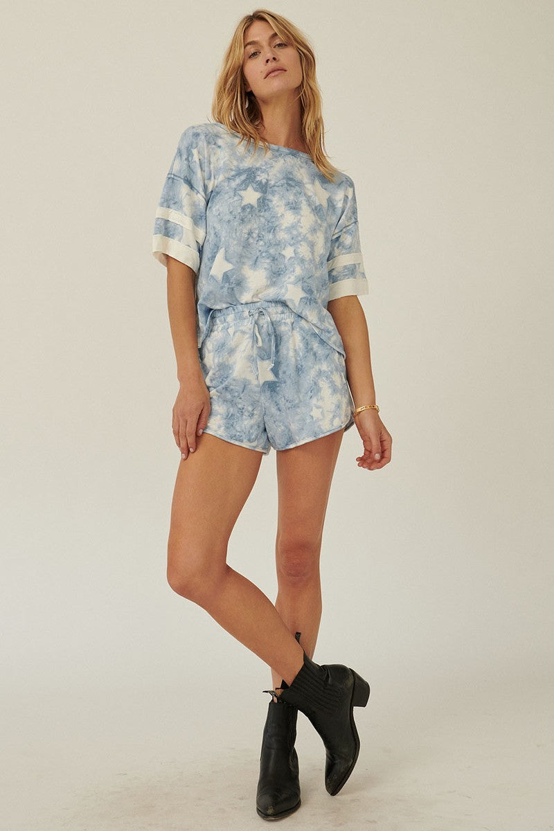 A blue star-pattern tie-dye knit top with short sleeves and varsity stripe trim, showcasing a relaxed oversized fit.