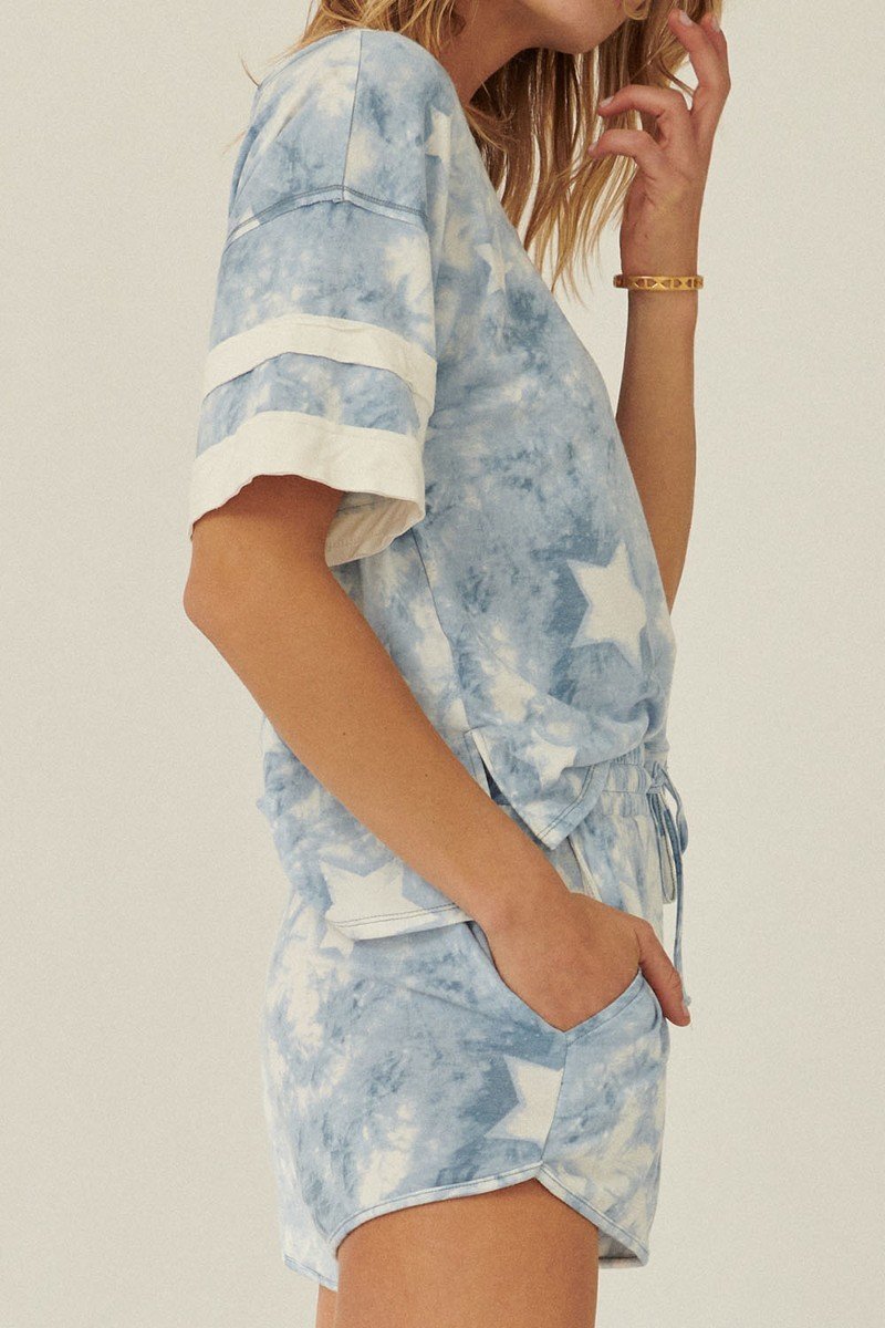 A blue star-pattern tie-dye knit top with short sleeves and varsity stripe trim, showcasing a relaxed oversized fit.