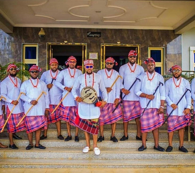 A complete set of African Groomsmen Attire including a shirt, wrapper, hat, necklace, bracelet, linking button stud, and staff, showcasing vibrant colors and traditional design.