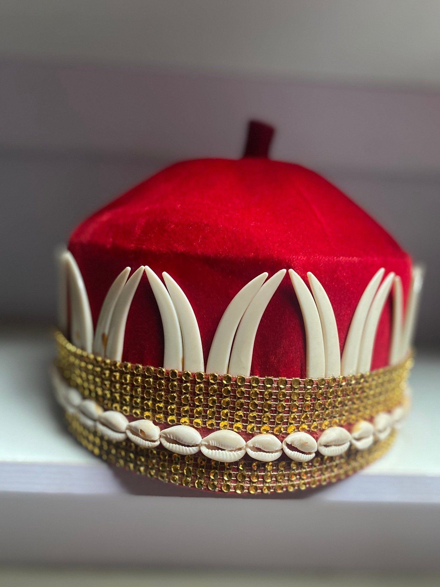 A vibrant red African hat embellished with cowries and tusks, symbolizing cultural heritage and elegance.