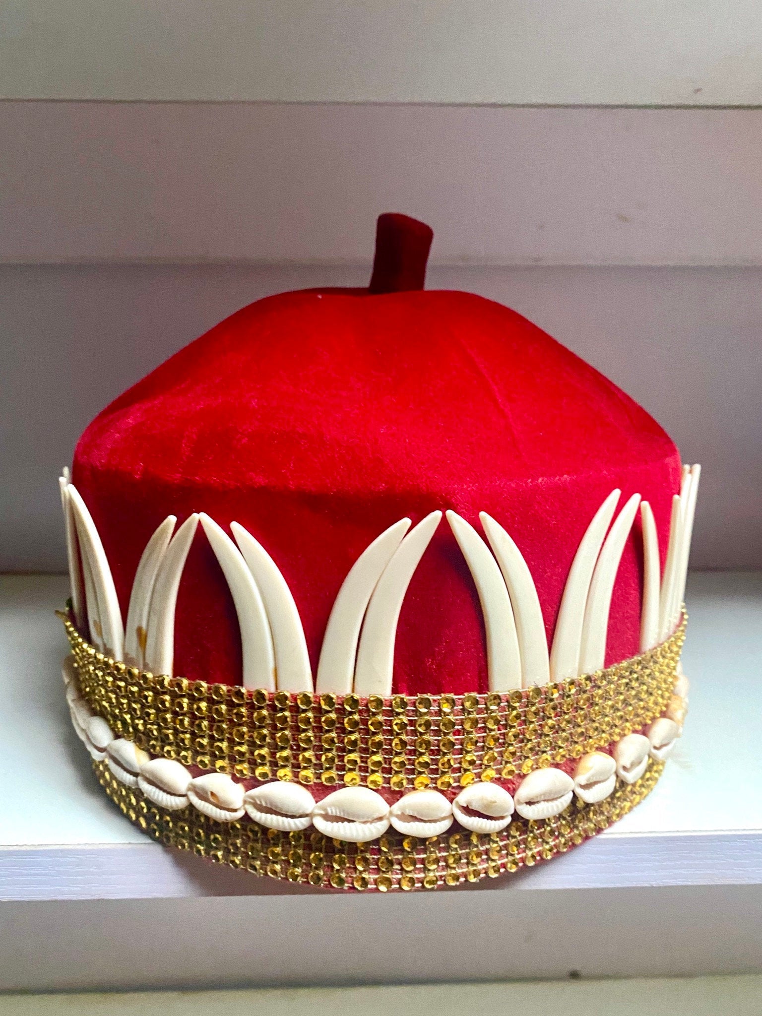 A vibrant red African hat embellished with cowries and tusks, symbolizing cultural heritage and elegance.