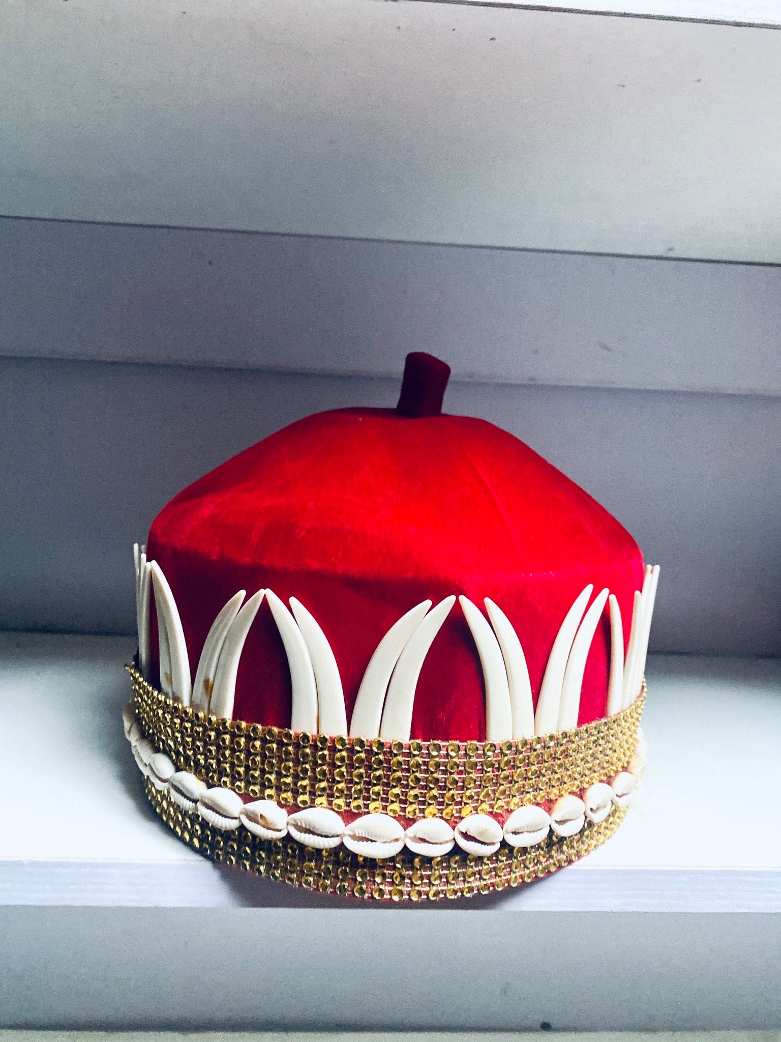 A vibrant red African hat embellished with cowries and tusks, symbolizing cultural heritage and elegance.