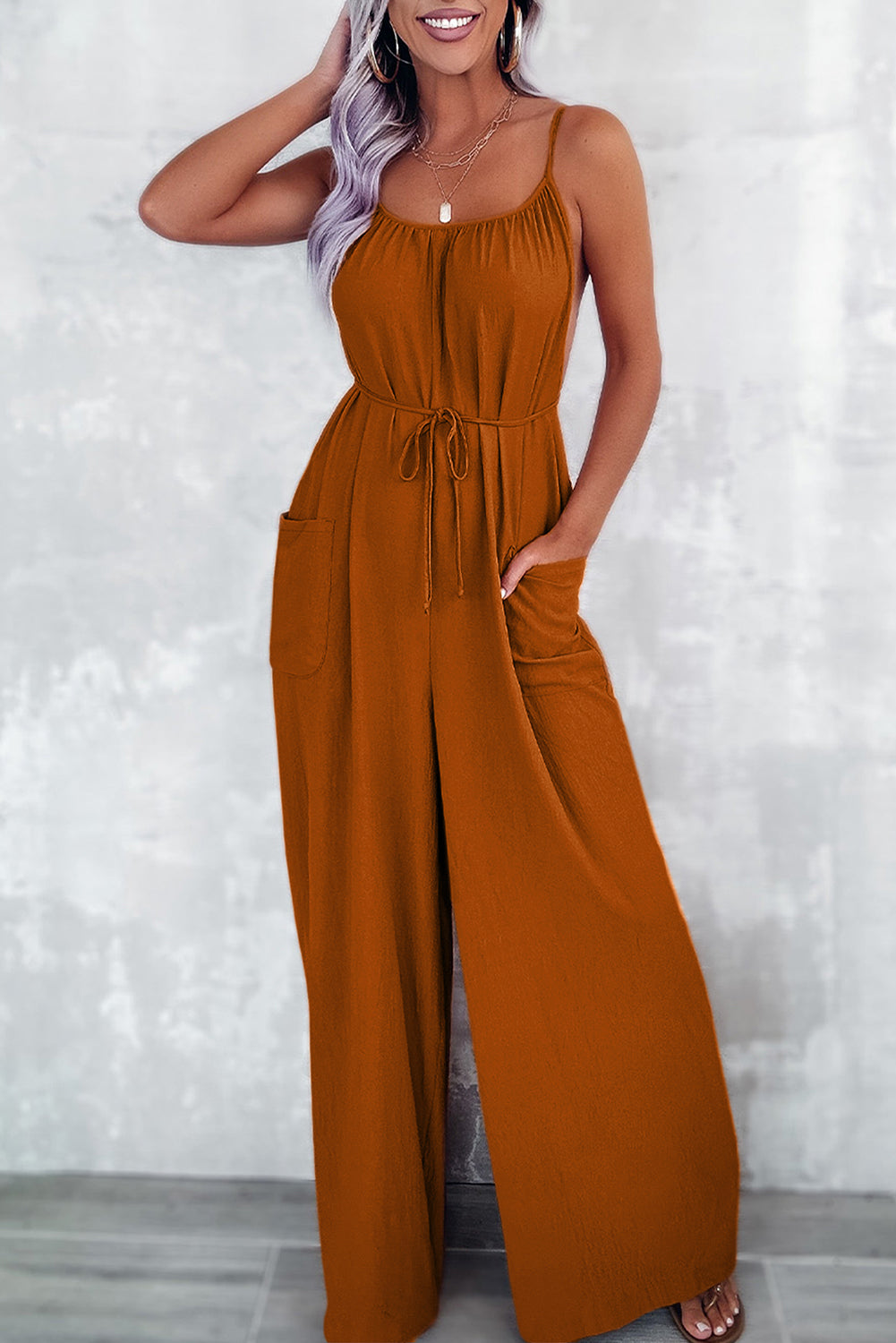 Apricot spaghetti straps jumpsuit with waist tie and pockets, featuring a wide leg design.