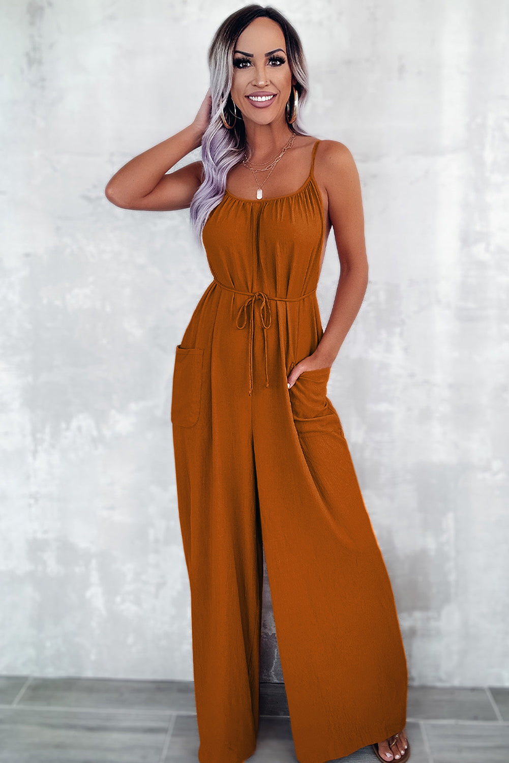 Apricot spaghetti straps jumpsuit with waist tie and pockets, featuring a wide leg design.