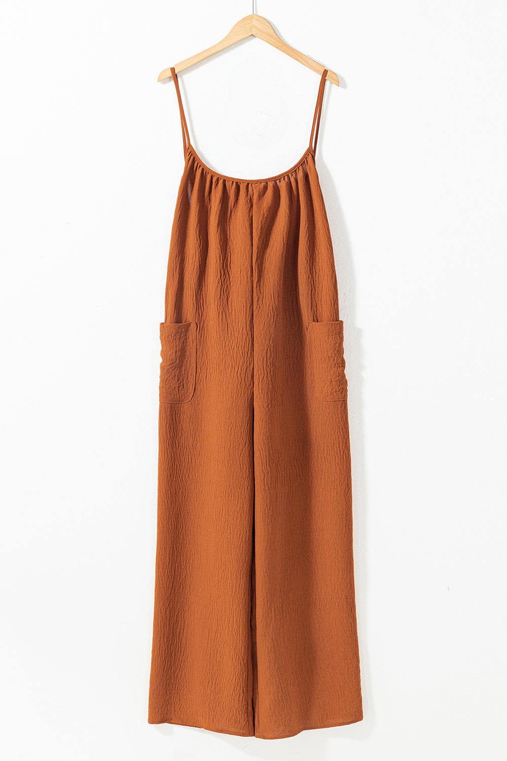 Apricot spaghetti straps jumpsuit with waist tie and pockets, featuring a wide leg design.