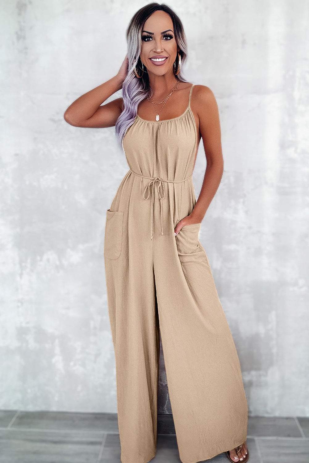 Apricot spaghetti straps jumpsuit with waist tie and pockets, featuring a wide leg design.