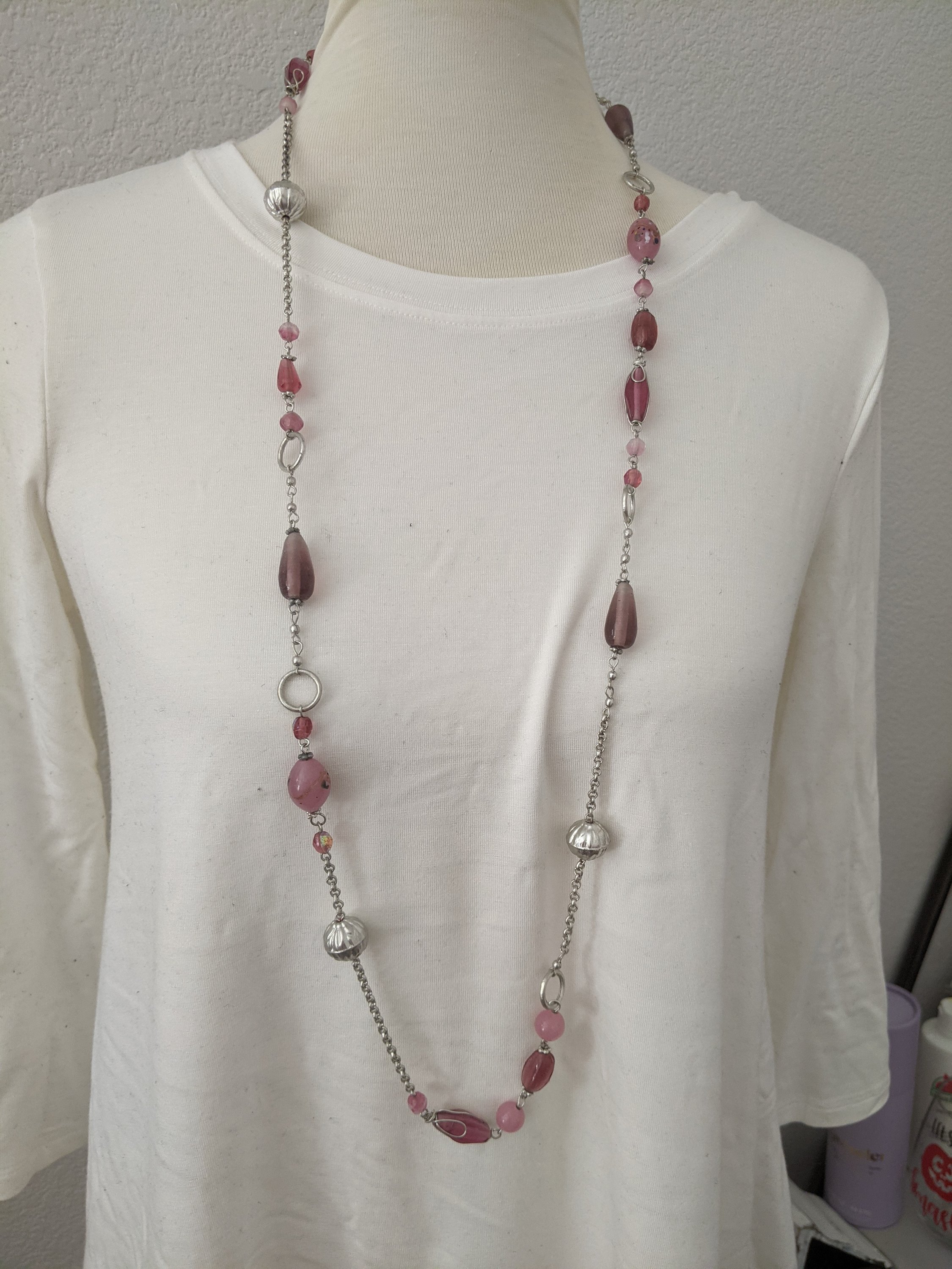 A long silver necklace adorned with beautiful pink stones, showcasing elegance and style.