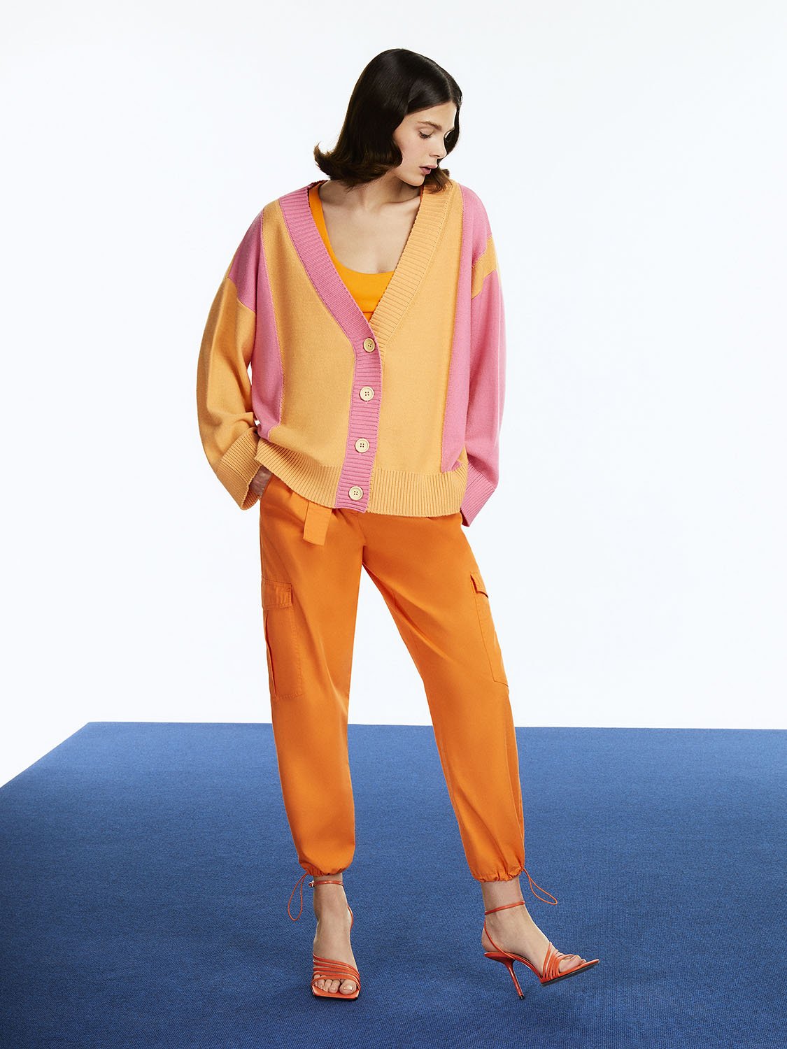 A pair of stylish belted cargo pants in vibrant orange, pink, and blue colors, featuring a high-waisted design and side flap pockets.