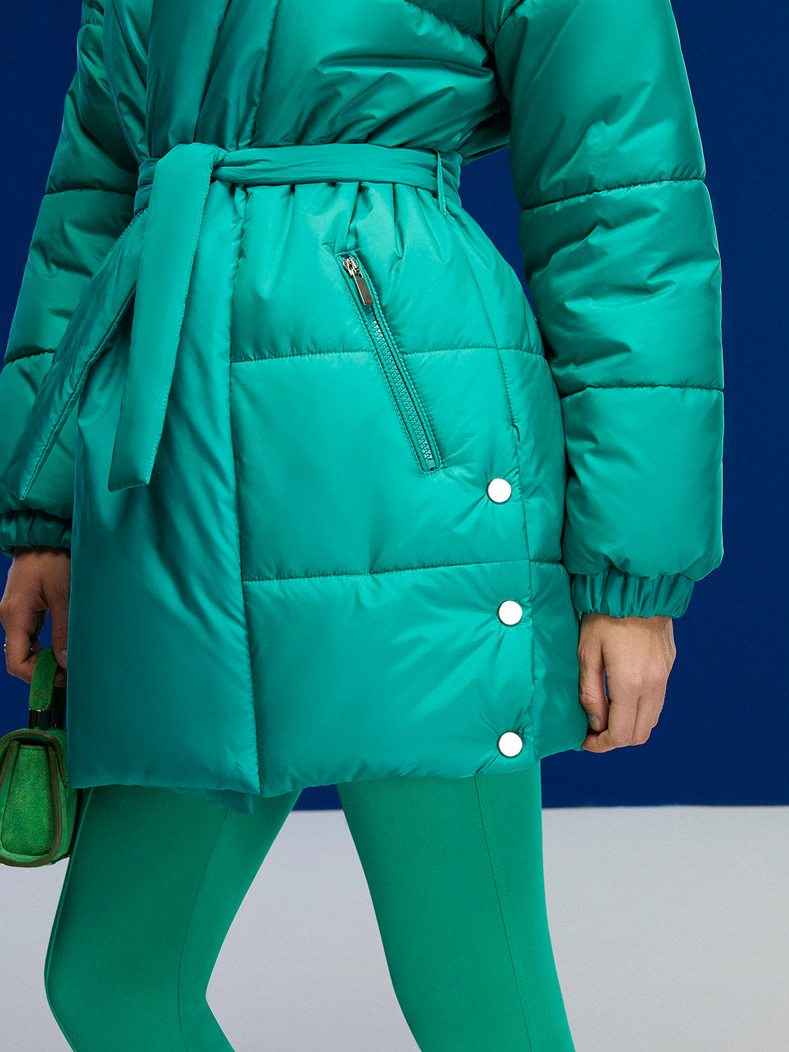 A stylish belted puffer jacket featuring a double-breasted design, wide neck, and side zipper pockets, perfect for cold weather fashion.