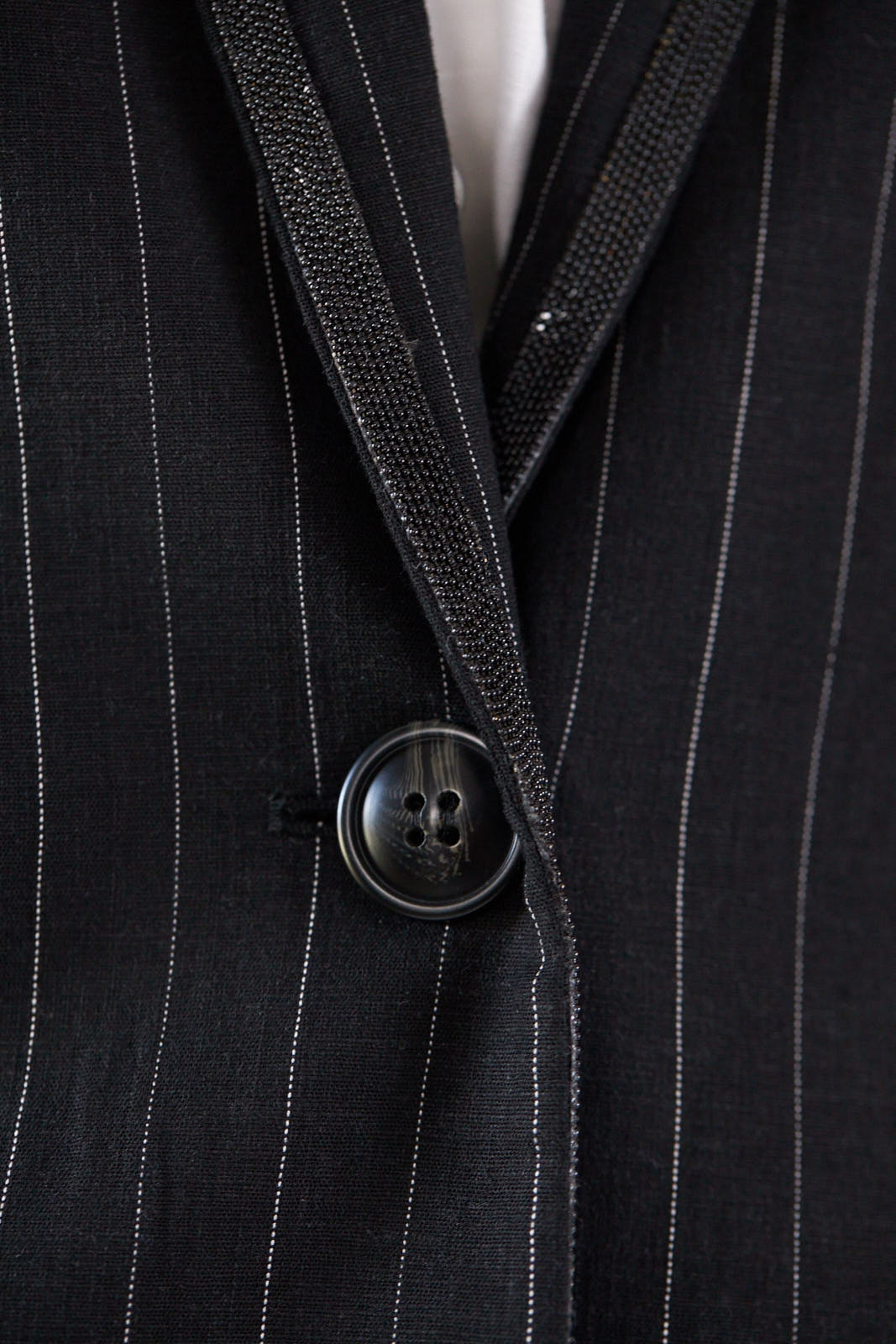 A stylish black blazer with white pinstripes, featuring designed lapels and a single button closure, perfect for professional and casual wear.