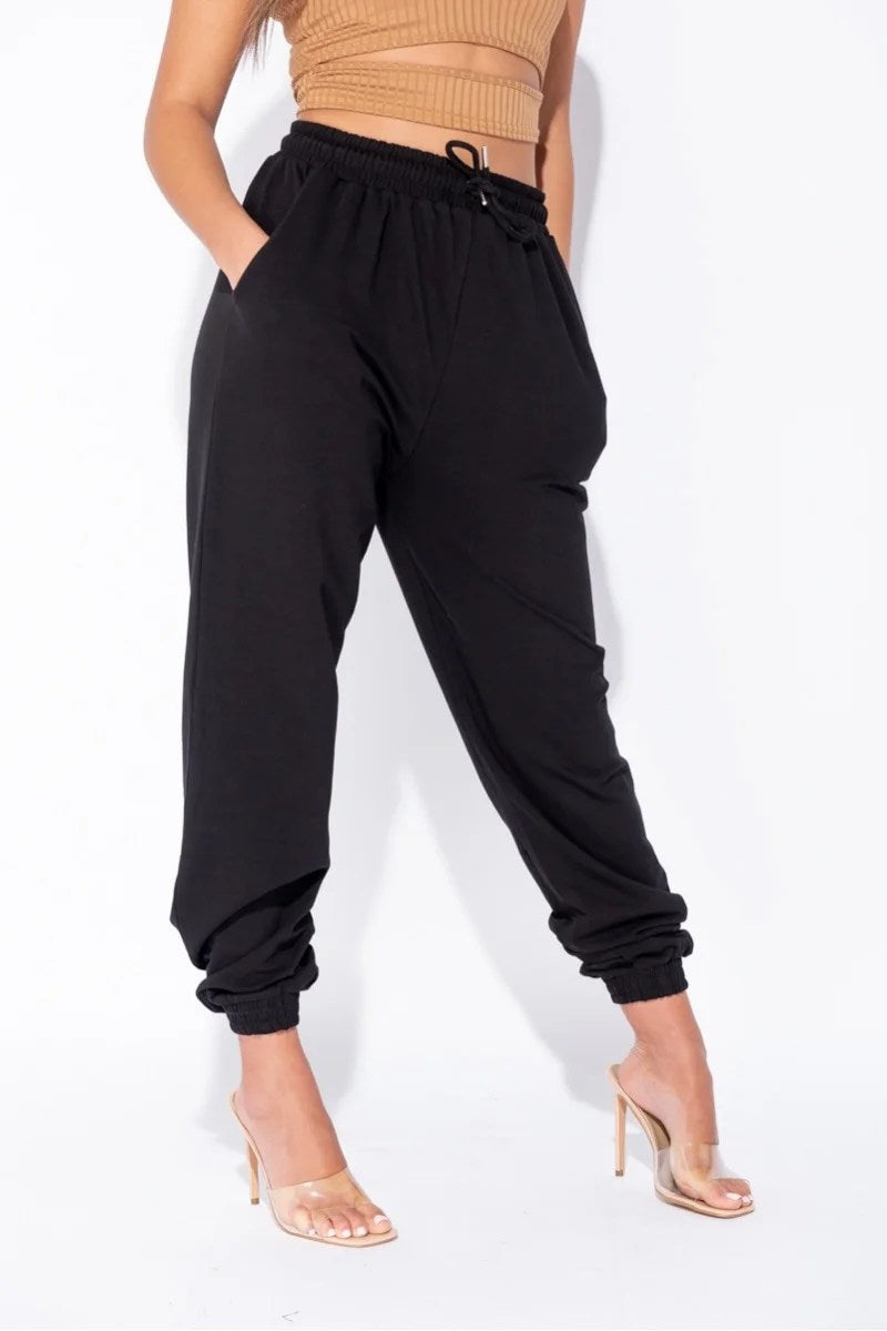 Black oversized joggers with a tie waist, featuring front pockets and a relaxed fit, perfect for casual wear.