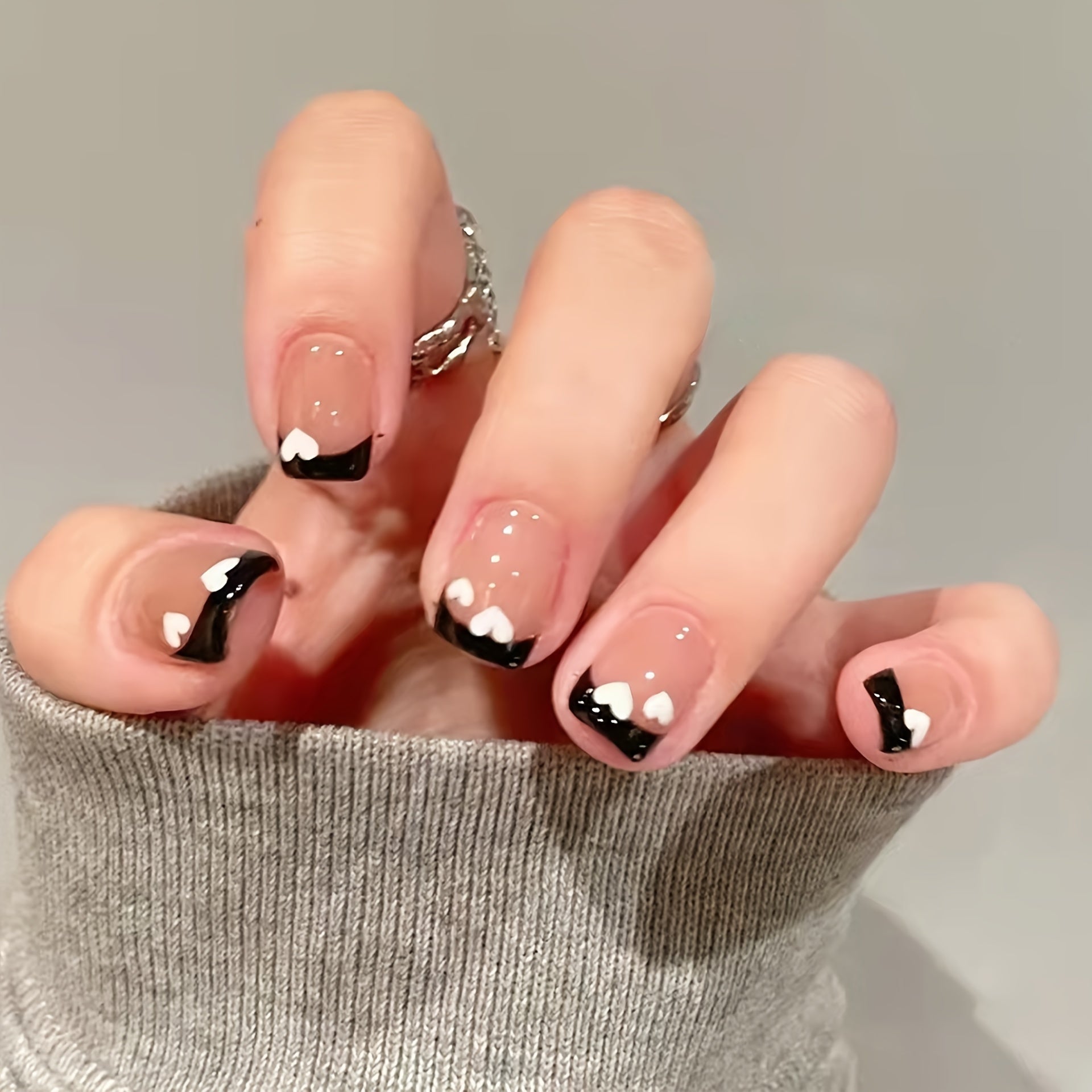 A set of Black & White Heart Nails featuring a shimmery finish and elegant oval shape, adorned with charming heart patterns.