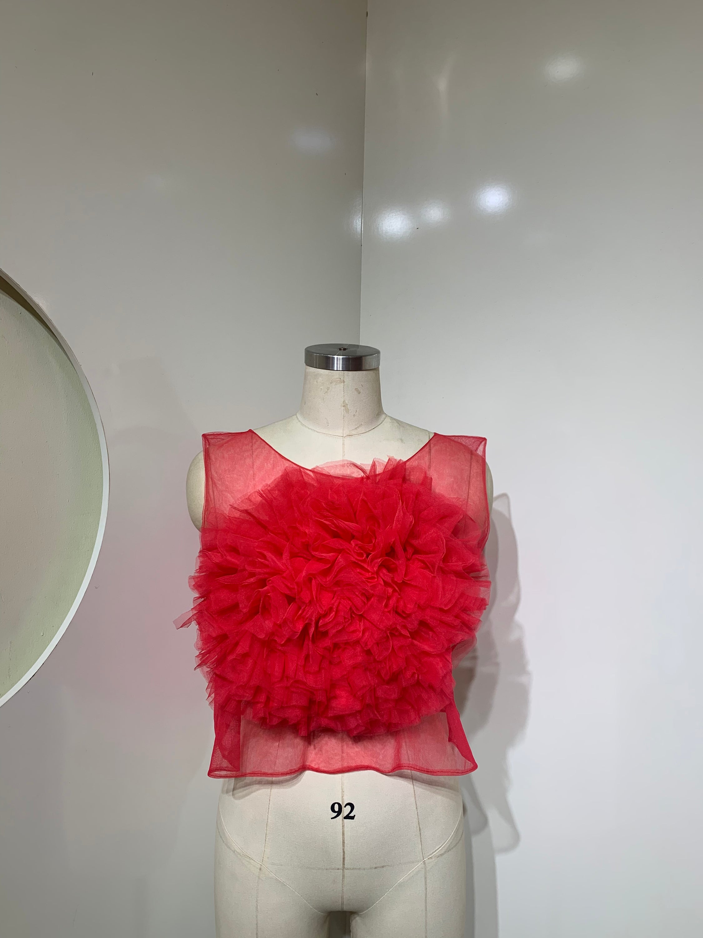 A vibrant red sheer tulle top featuring a playful ruffled flower detail at the center, perfect for stylish occasions.