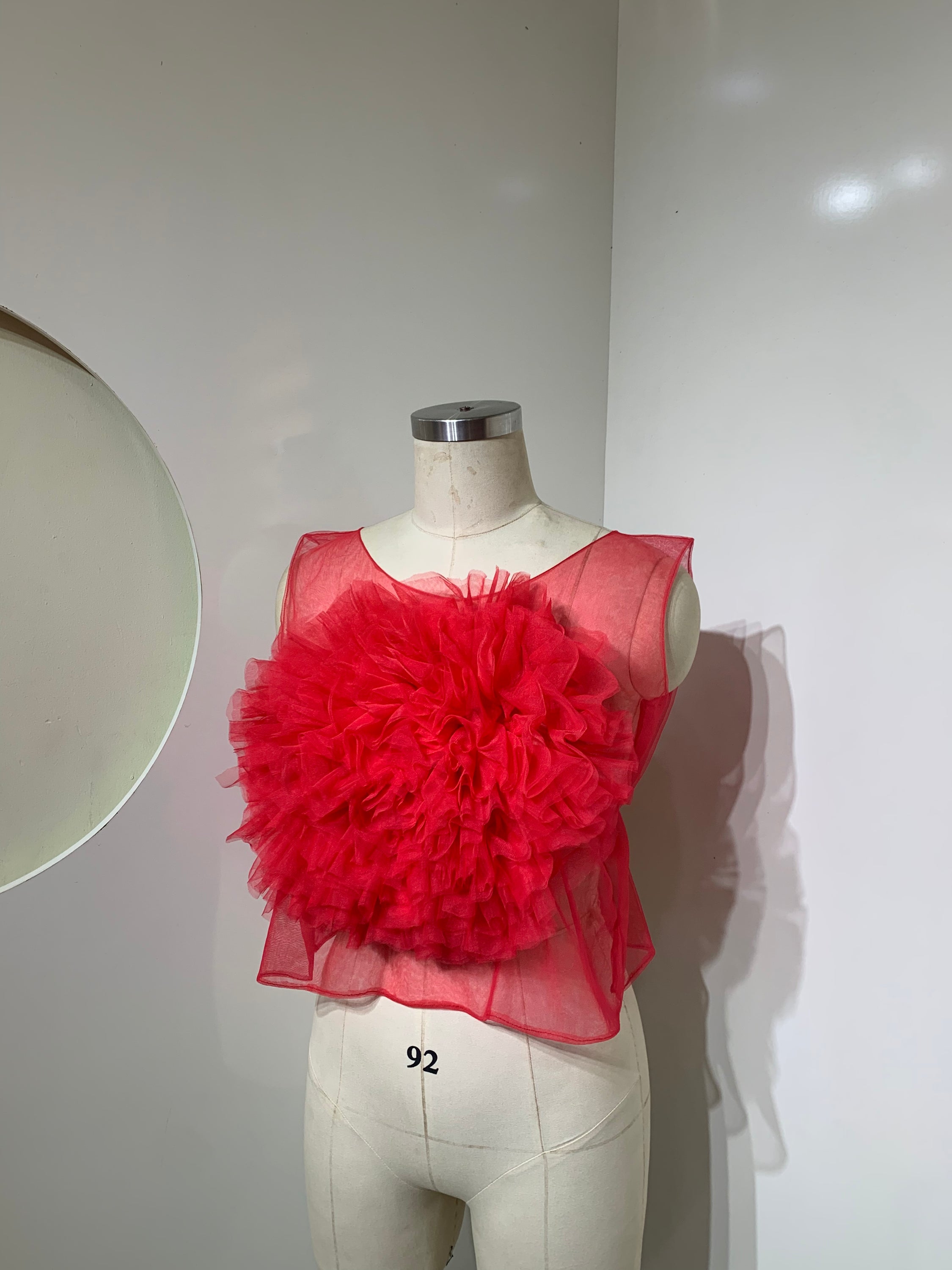 A vibrant red sheer tulle top featuring a playful ruffled flower detail at the center, perfect for stylish occasions.