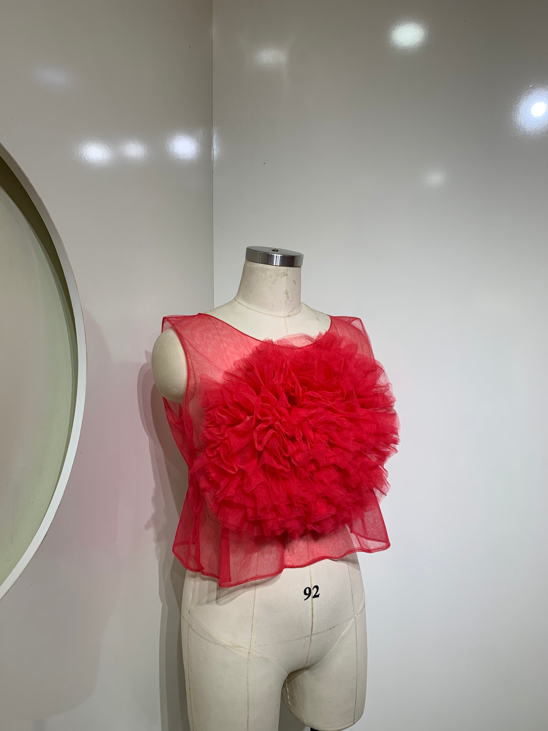 A vibrant red sheer tulle top featuring a playful ruffled flower detail at the center, perfect for stylish occasions.