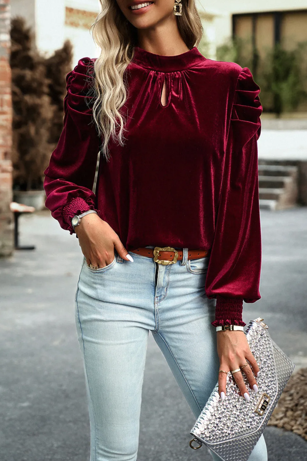 Elegant red blouse made of imitation velvet with high neck and long puffed sleeves, featuring a decorative bow at the neckline.