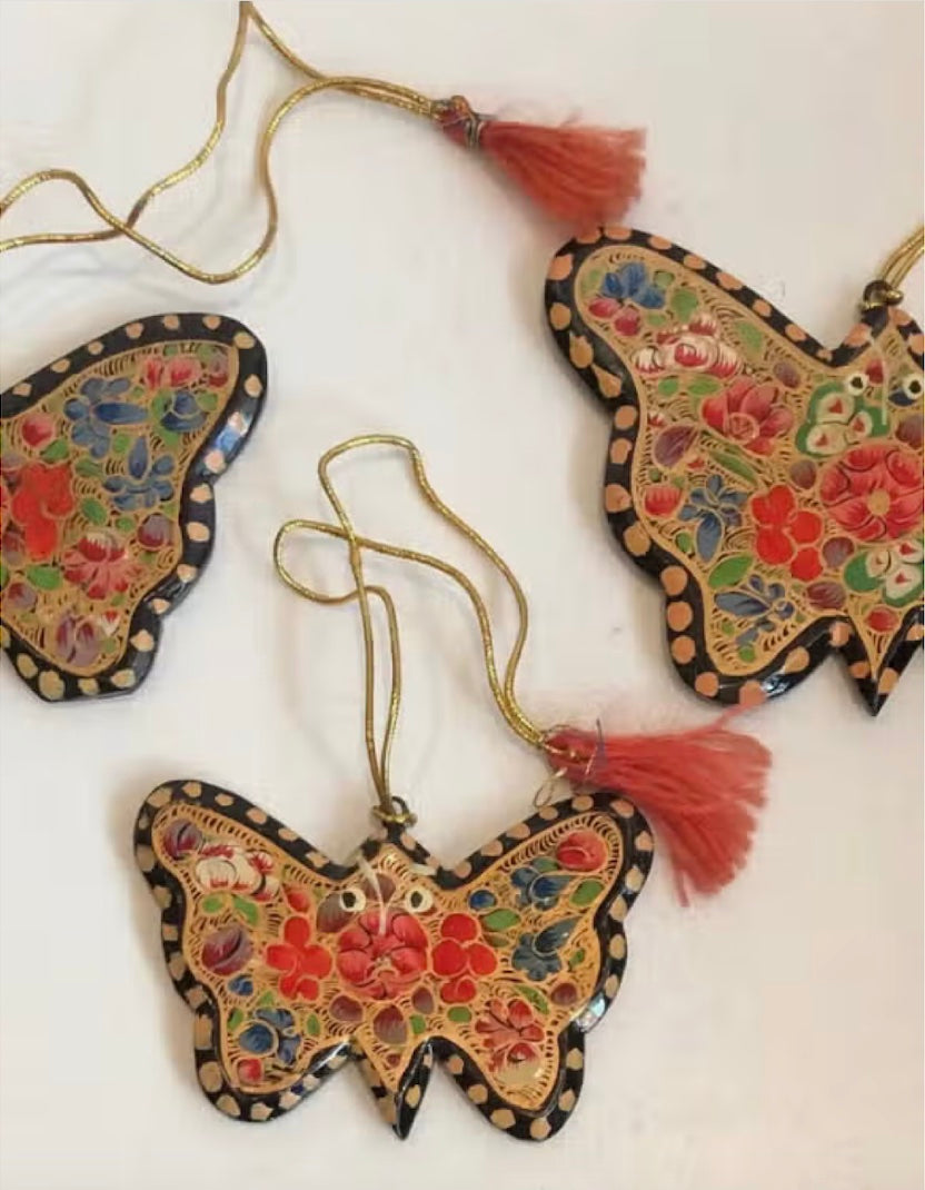 A collection of beautifully hand-painted butterly shaped holiday ornaments, showcasing vibrant colors and intricate designs, crafted from recycled paper.