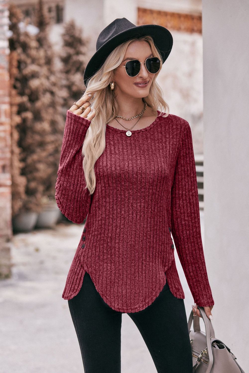 A stylish Buttoned Hem Detail Ribbed Top featuring a round neck, long sleeves, and a unique buttoned hem design in a solid color.