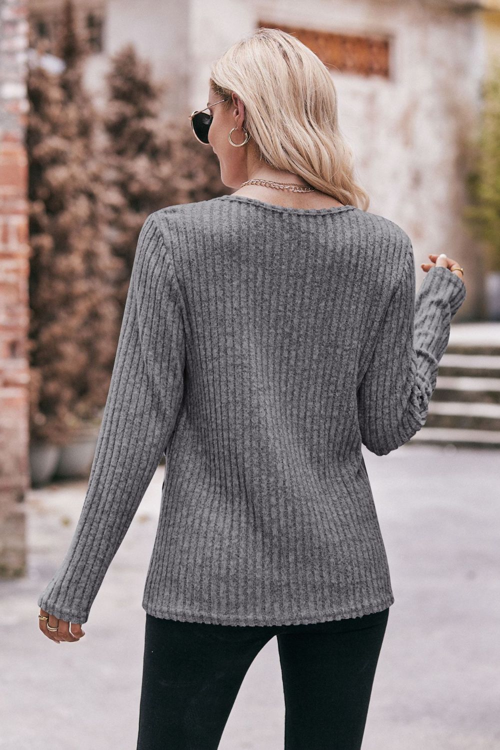 A stylish Buttoned Hem Detail Ribbed Top featuring a round neck, long sleeves, and a unique buttoned hem design in a solid color.