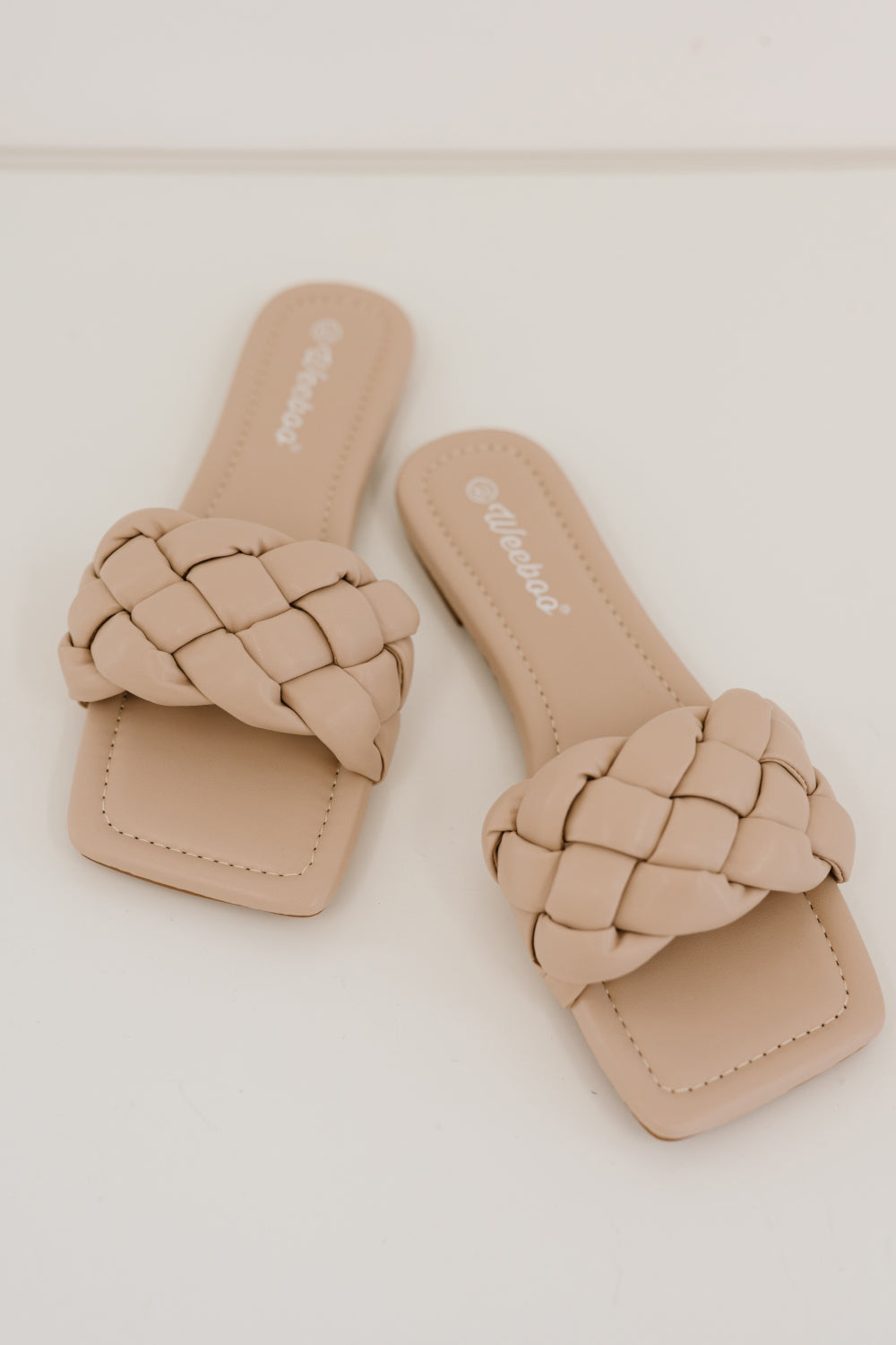 A pair of Cakewalk Woven Square Toe Slides featuring a chic woven strap and square toe design, made from vegan leather.