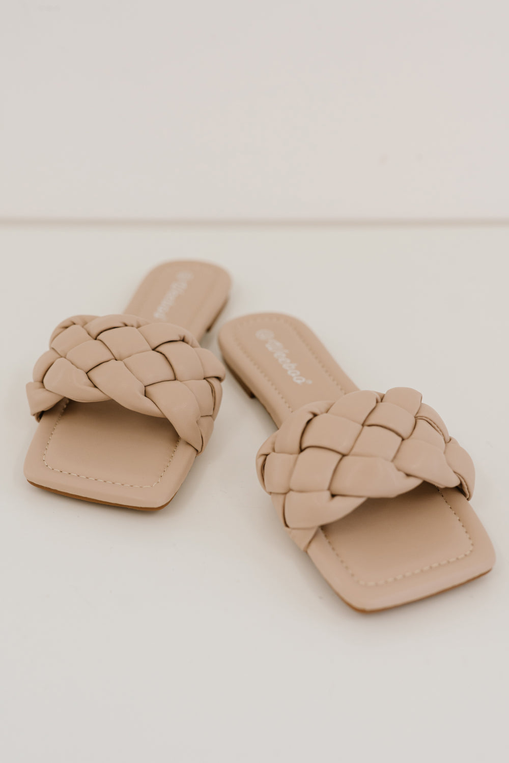 A pair of Cakewalk Woven Square Toe Slides featuring a chic woven strap and square toe design, made from vegan leather.