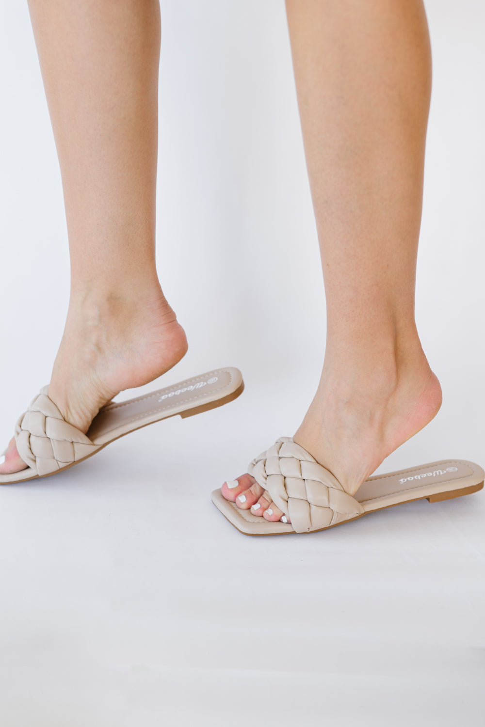 A pair of Cakewalk Woven Square Toe Slides featuring a chic woven strap and square toe design, made from vegan leather.