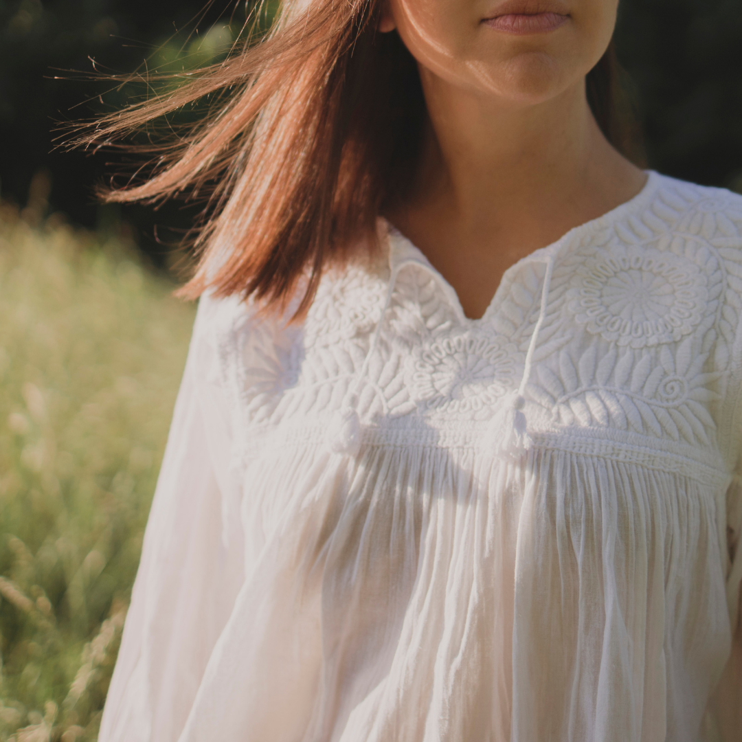 Chaya Blouse featuring white cotton fabric with intricate hand embroidery and tassel details on sleeves.