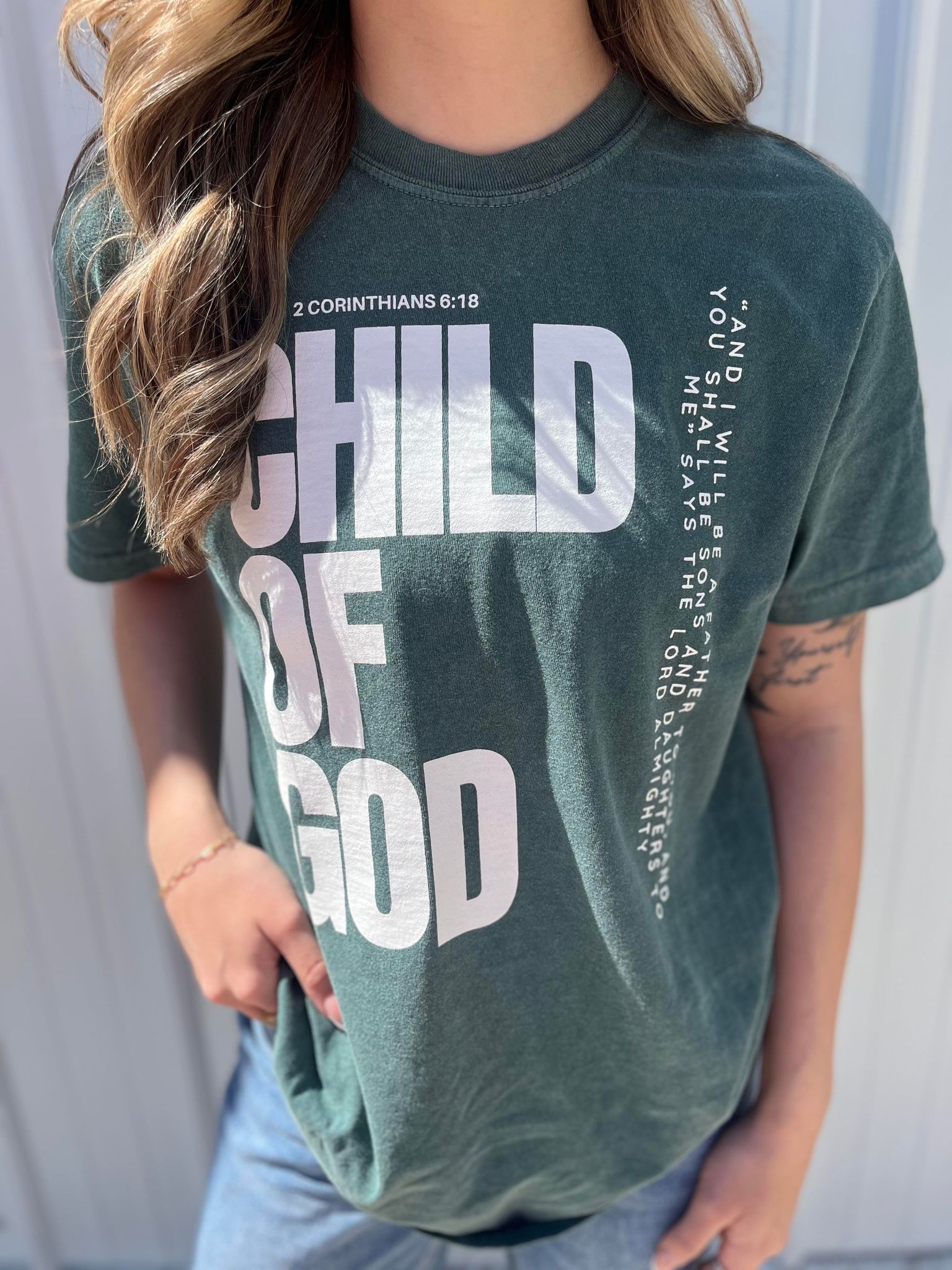 A stylish blue spruce Child of God Tee made from 100% cotton, featuring a bold screen-printed design.