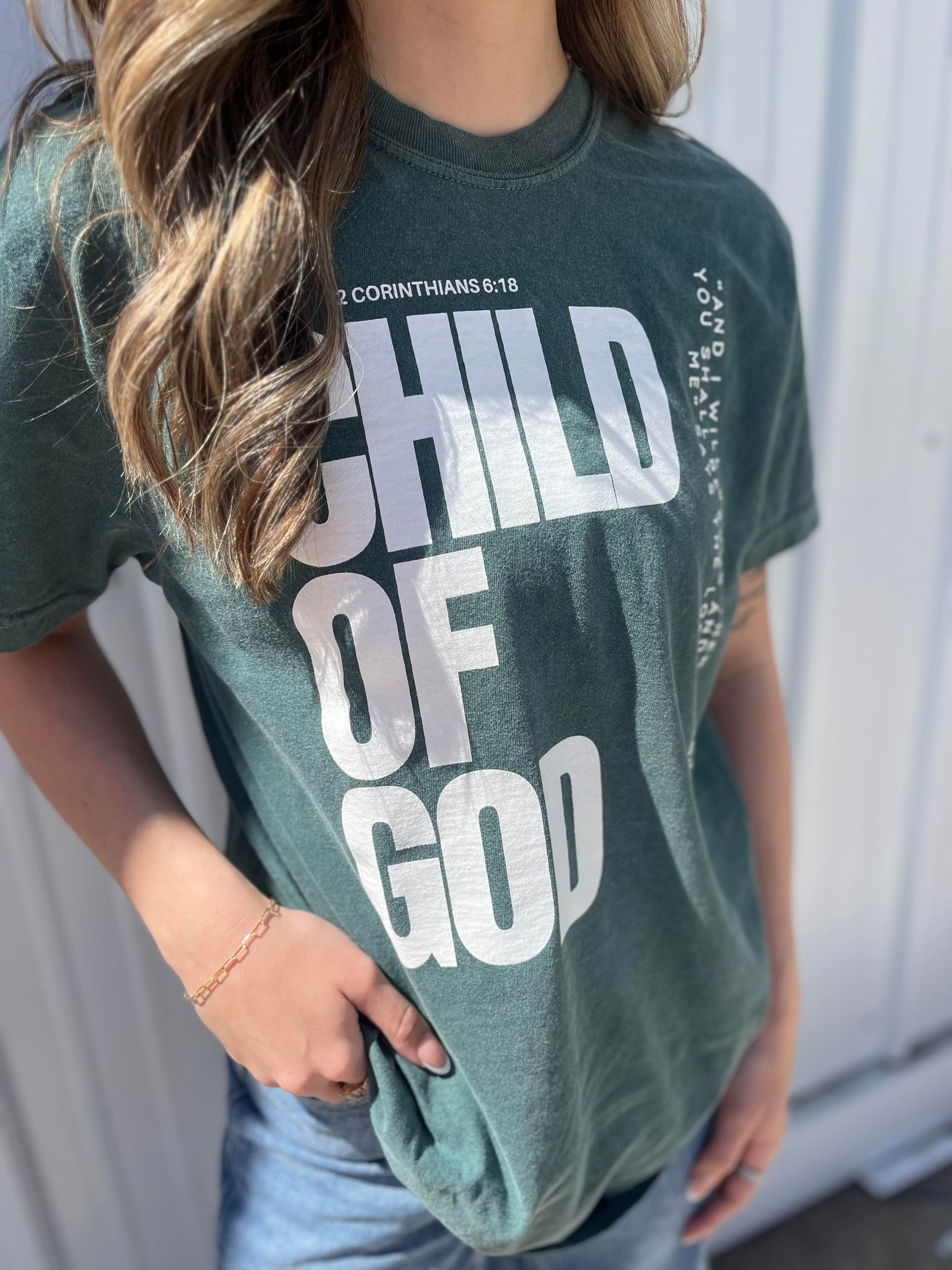 A stylish blue spruce Child of God Tee made from 100% cotton, featuring a bold screen-printed design.