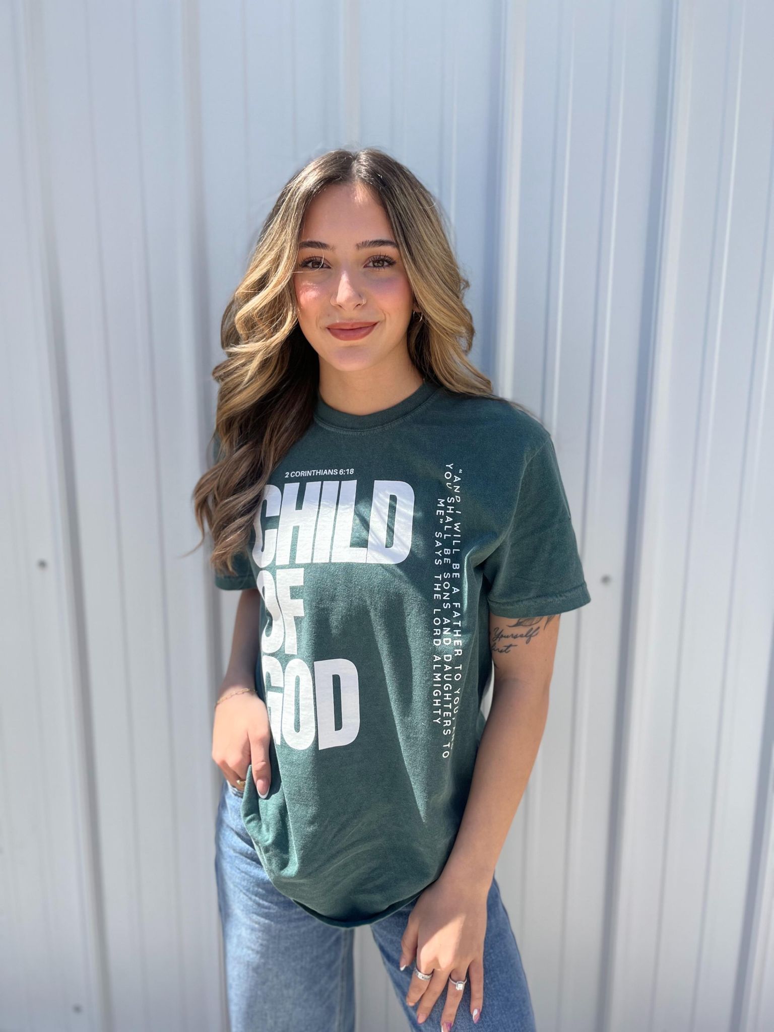 A stylish blue spruce Child of God Tee made from 100% cotton, featuring a bold screen-printed design.