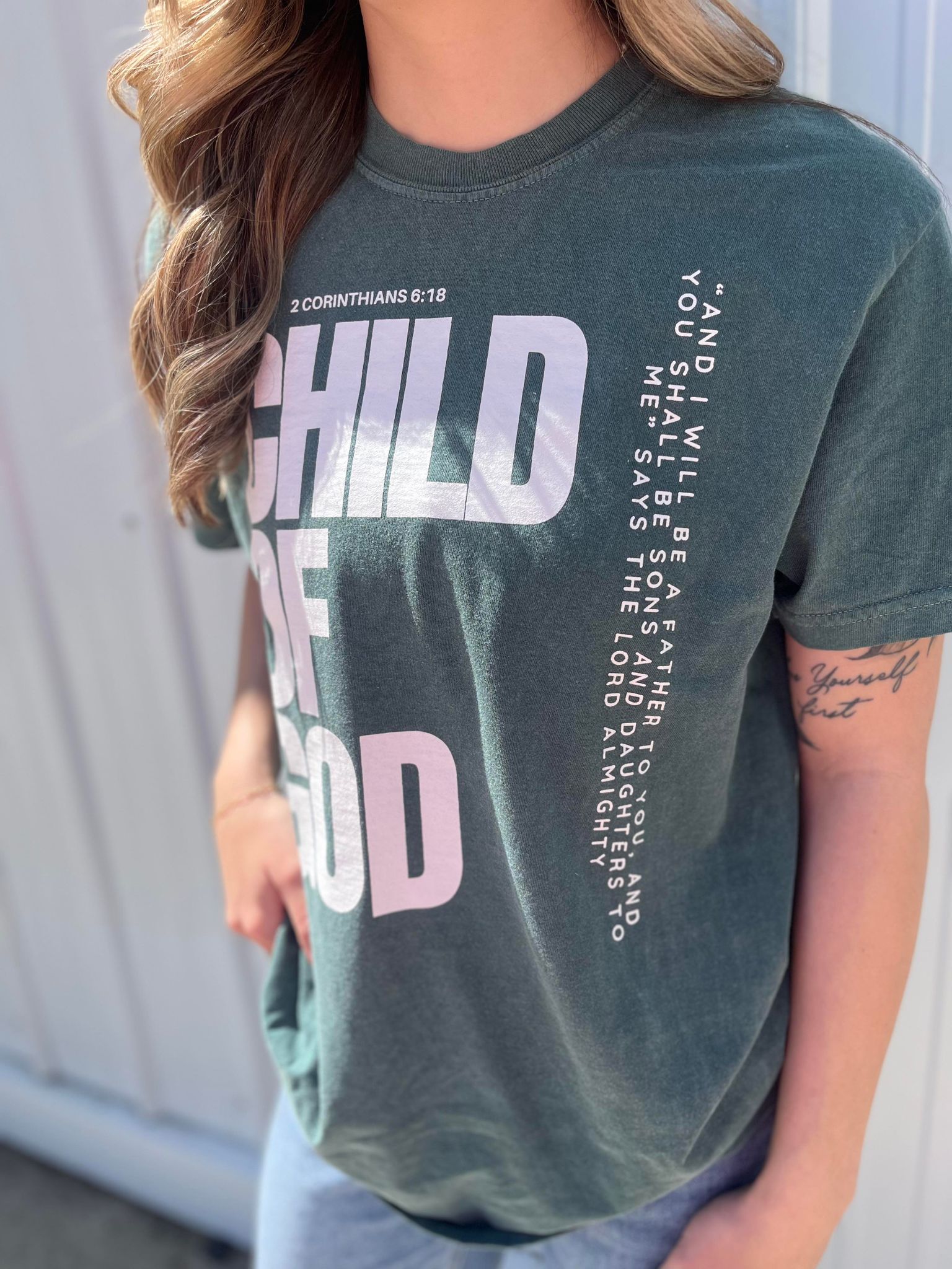 A stylish blue spruce Child of God Tee made from 100% cotton, featuring a bold screen-printed design.