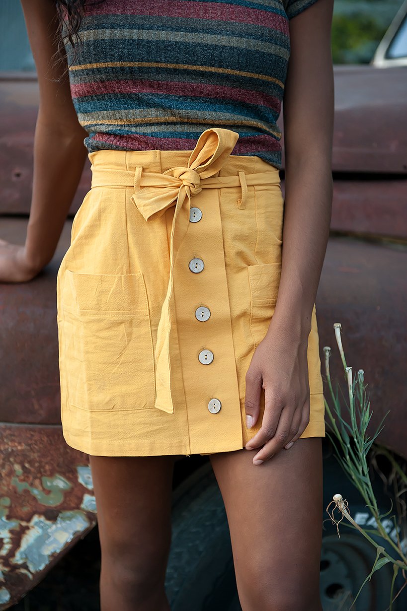 Coconut Button Solid Woven Skirt in Mustard with belt and accent pockets, displayed on a model.