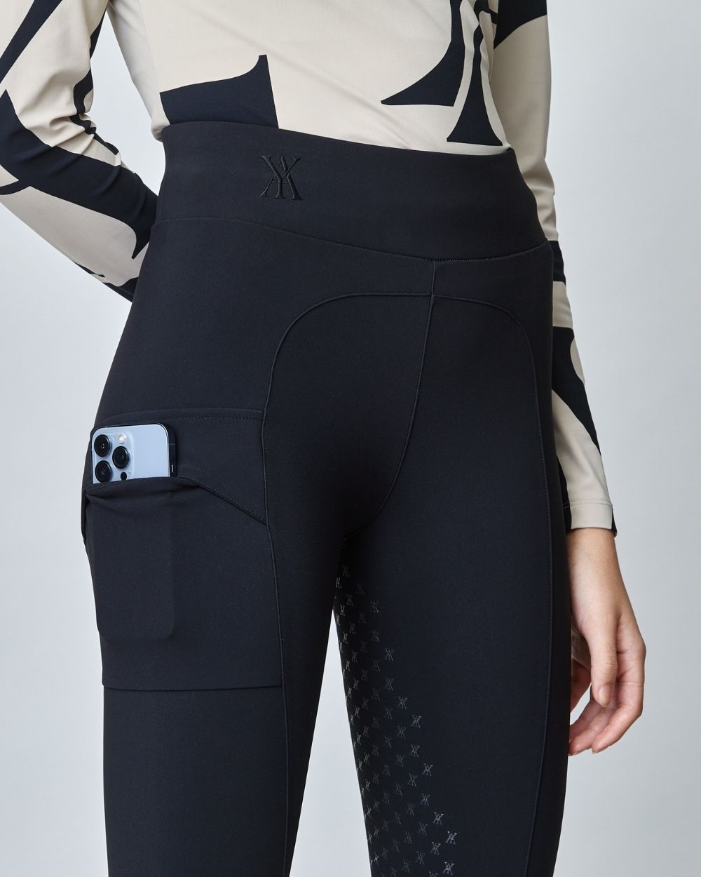 A pair of black compression pull-on breeches designed for equestrian riding, featuring a high waist and discreet mobile phone pocket.