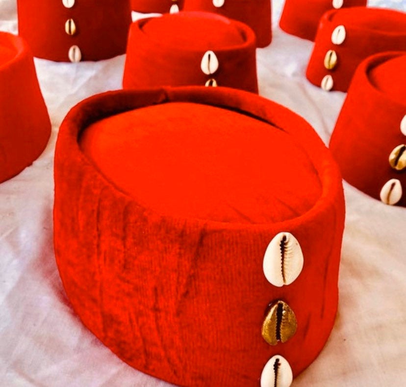 A vibrant red Cowries African hat adorned with decorative cowrie shells, showcasing its unique design and craftsmanship.