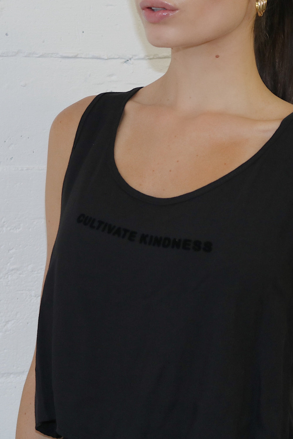 A stylish black cropped tank top with the phrase 'Cultivate Kindness' printed, showcasing a relaxed fit and lightweight fabric.