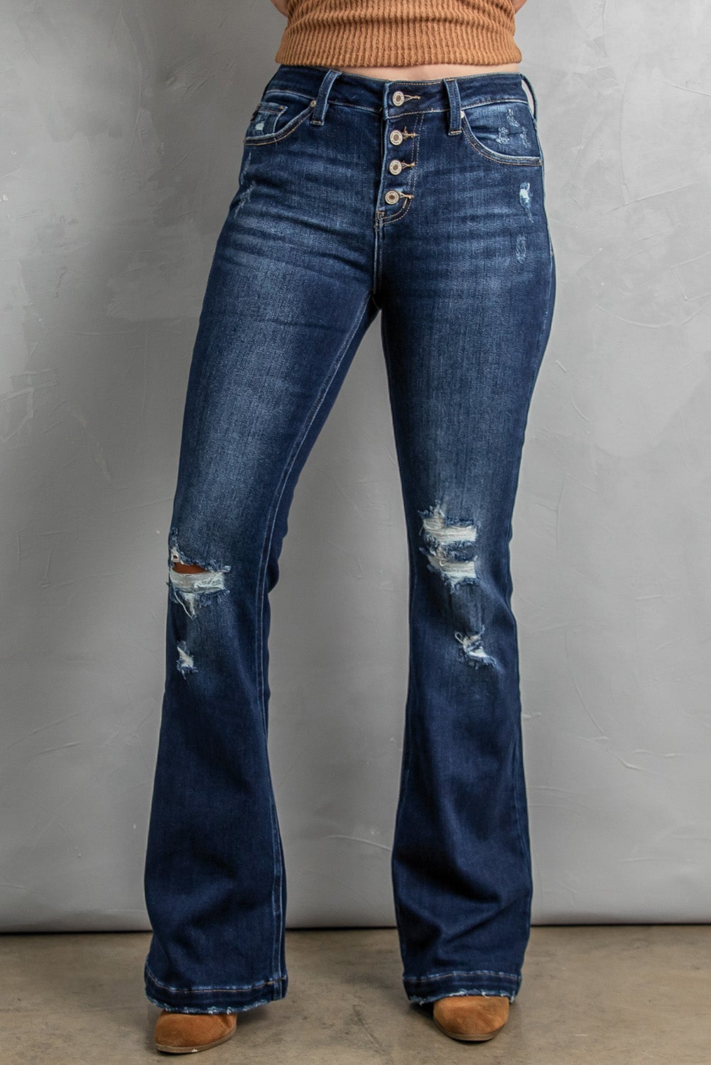 A pair of distressed flare bottom jeans featuring a medium wash, frayed hem, and 4-button closure, styled on a mannequin.