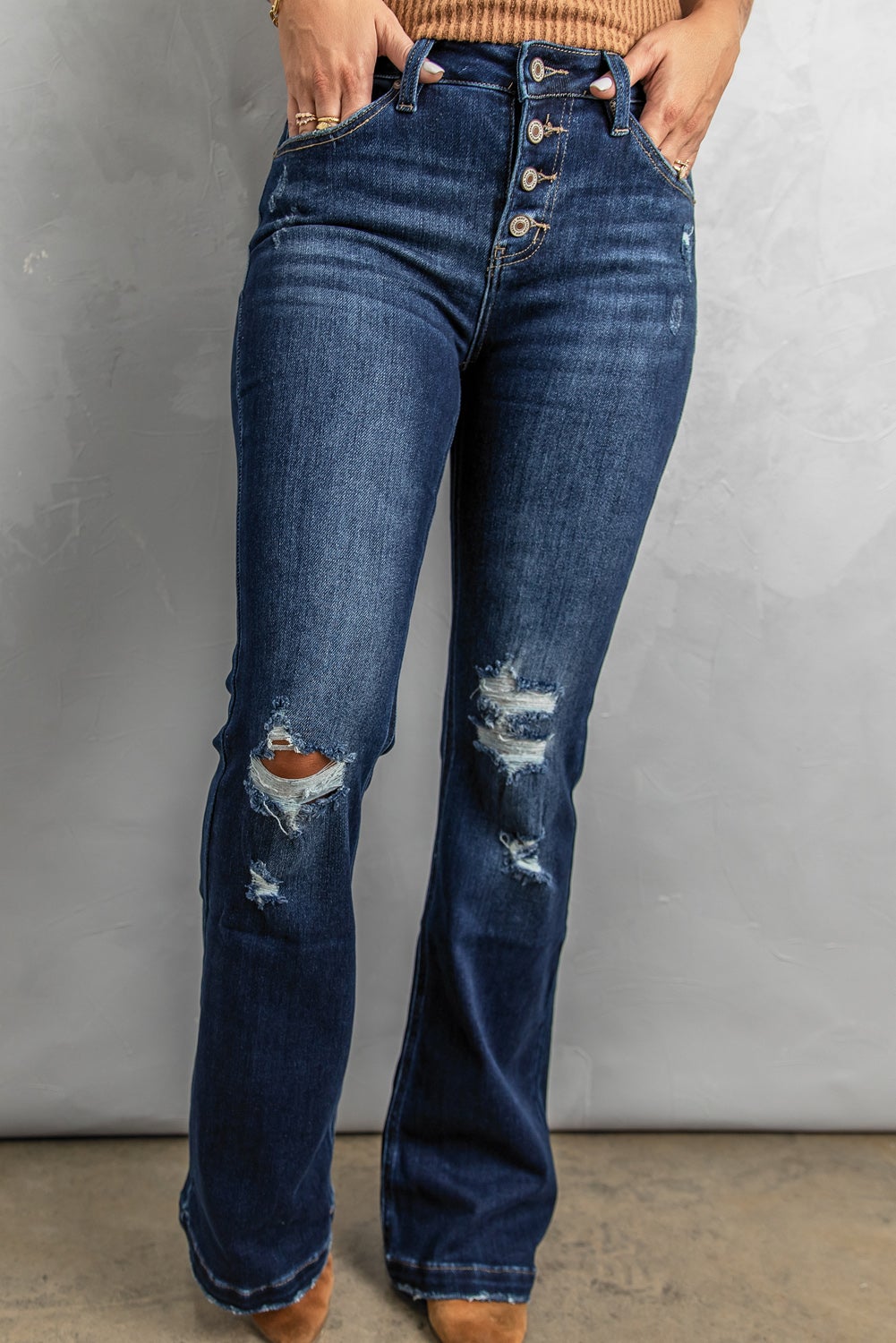 A pair of distressed flare bottom jeans featuring a medium wash, frayed hem, and 4-button closure, styled on a mannequin.