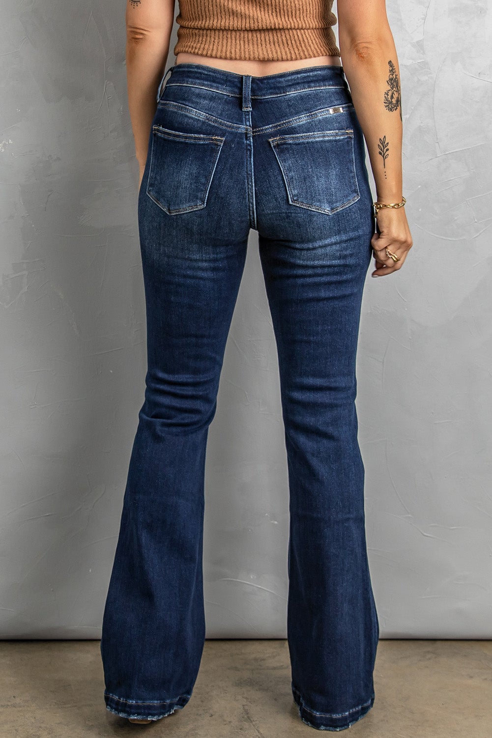 A pair of distressed flare bottom jeans featuring a medium wash, frayed hem, and 4-button closure, styled on a mannequin.