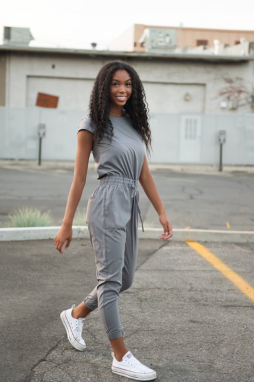 DT UNITY Jumpsuit in Cement featuring cap sleeves, adjustable tie waist, and pockets, displayed on a model.