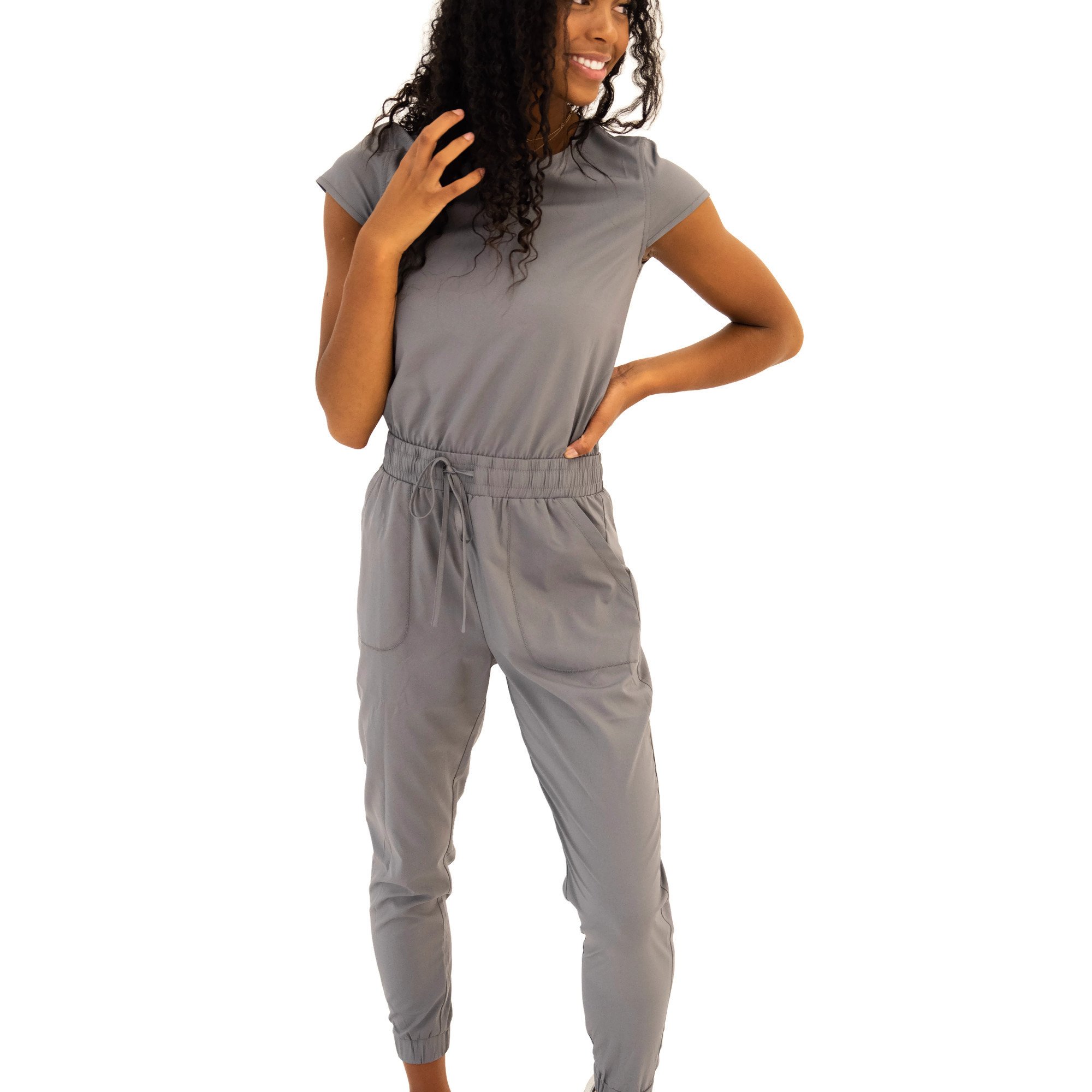 DT UNITY Jumpsuit in Cement featuring cap sleeves, adjustable tie waist, and pockets, displayed on a model.