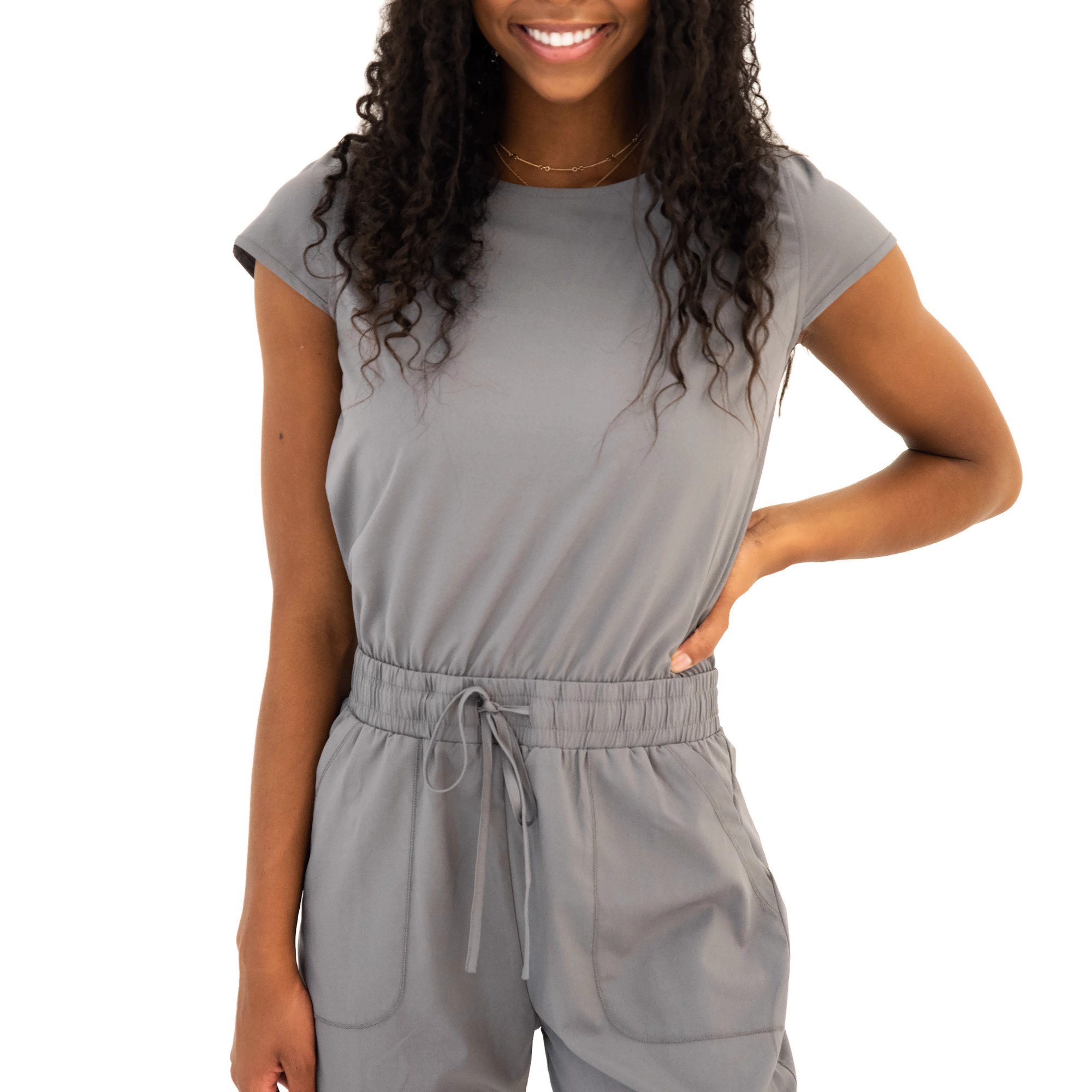 DT UNITY Jumpsuit in Cement featuring cap sleeves, adjustable tie waist, and pockets, displayed on a model.