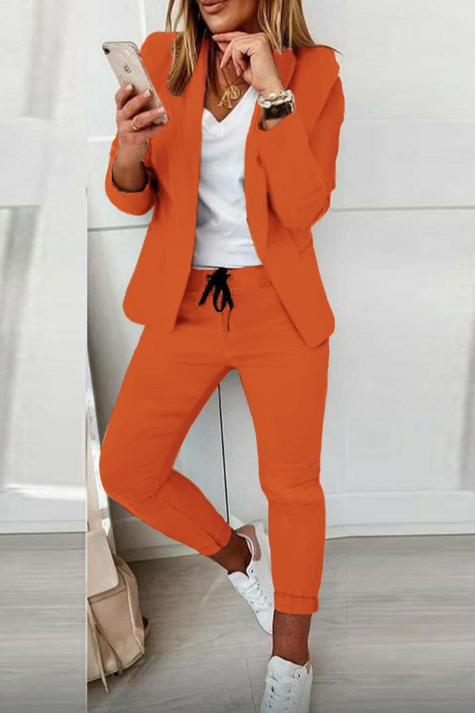 Elegant orange blazer and pants set Estrena, showcasing a classic collar, long sleeves, and fitted trousers with a drawstring waist.