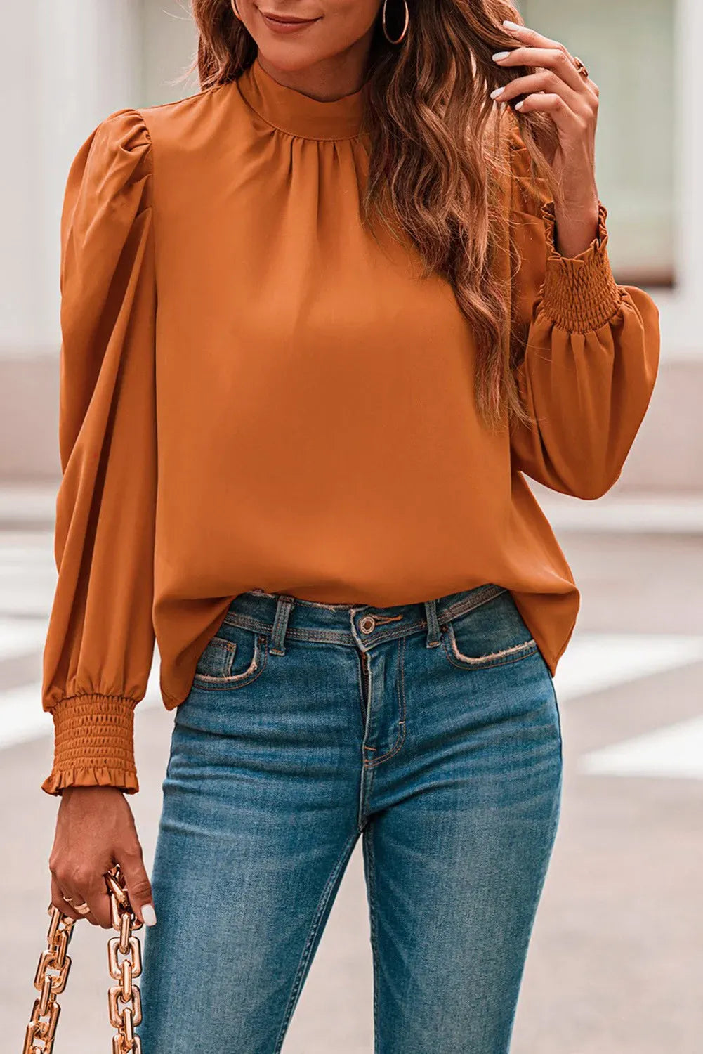 Elegant orange blouse with high neck and long sleeves, featuring a loose fit and cuffed wrists.