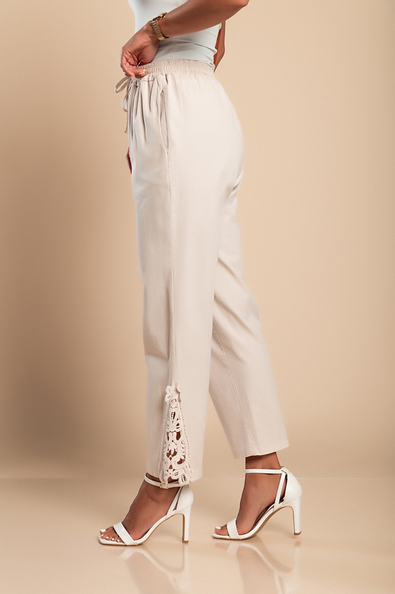 Elegant beige cotton trousers with lace detailing, featuring an elastic and drawstring waist, designed for comfort and style.