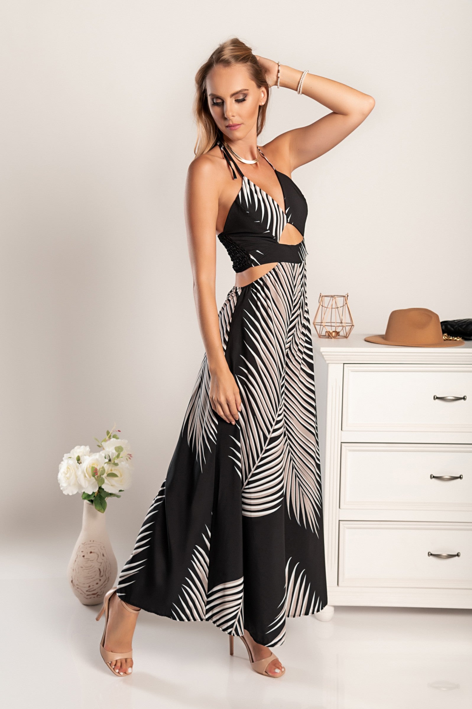 Elegant black jumpsuit with palm leaf print, featuring a plunging neckline, slim straps, and stylish cutouts on the belly and sides.